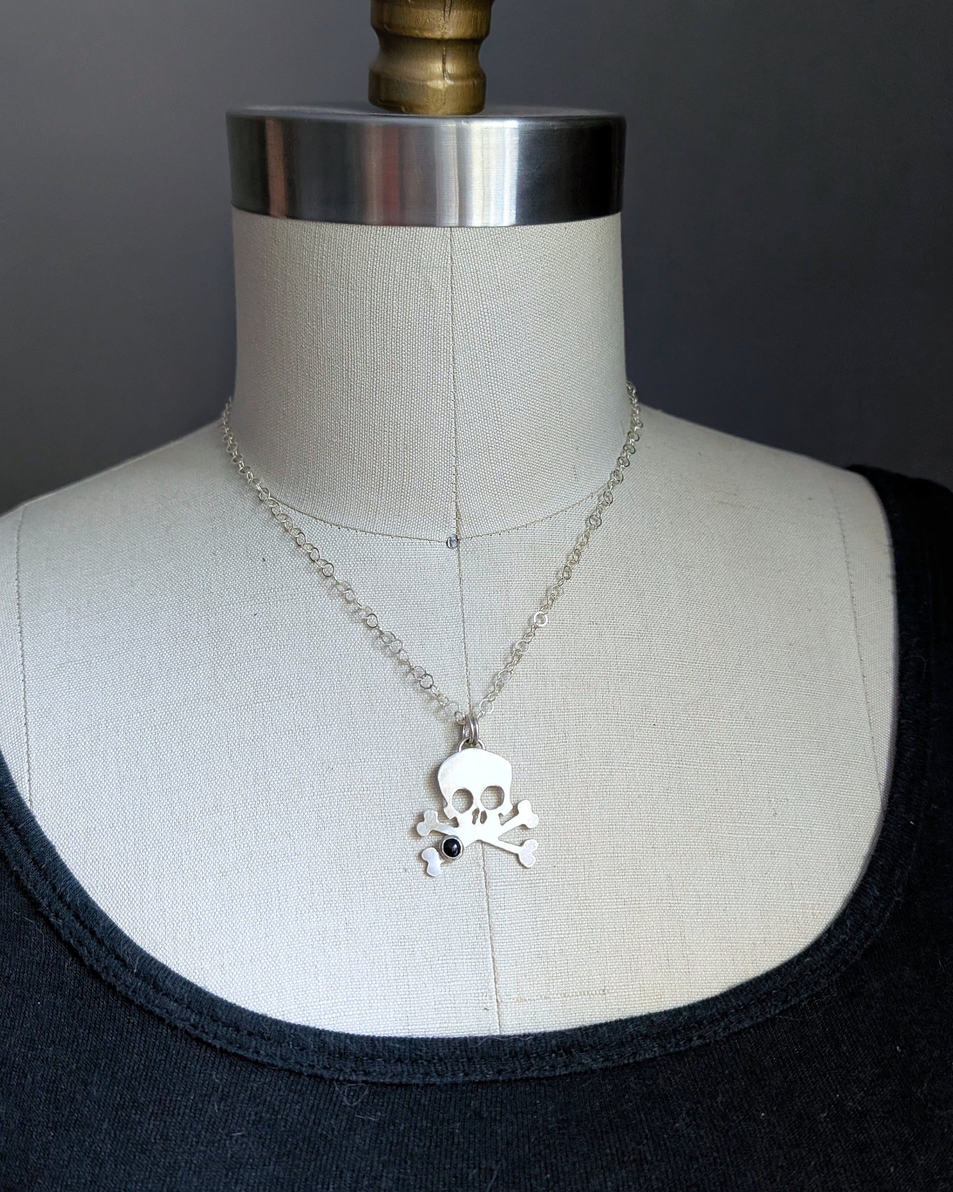 Skull and crossbones necklace on a mannequin with a dark background