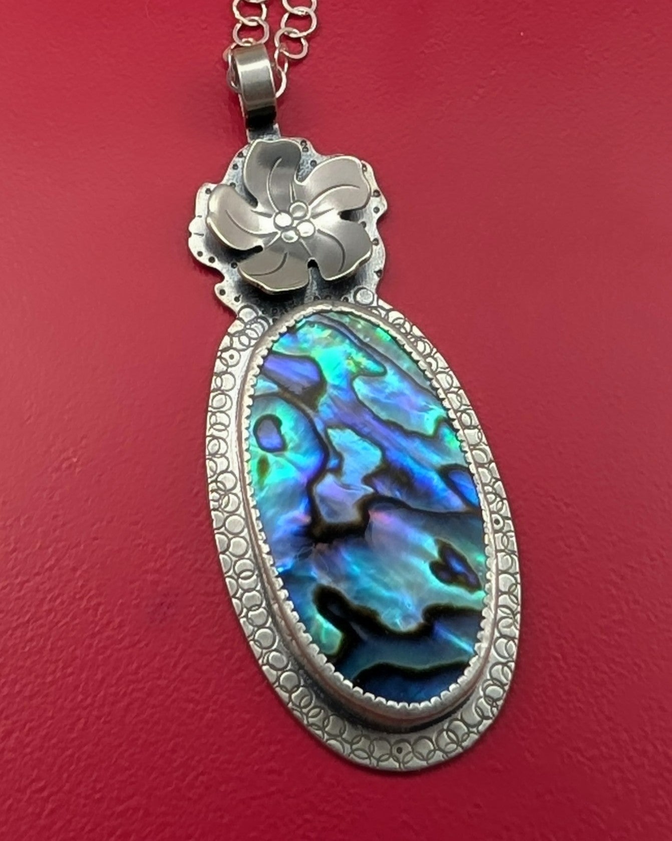 Abalone shell necklace with sterling silver flower on red background