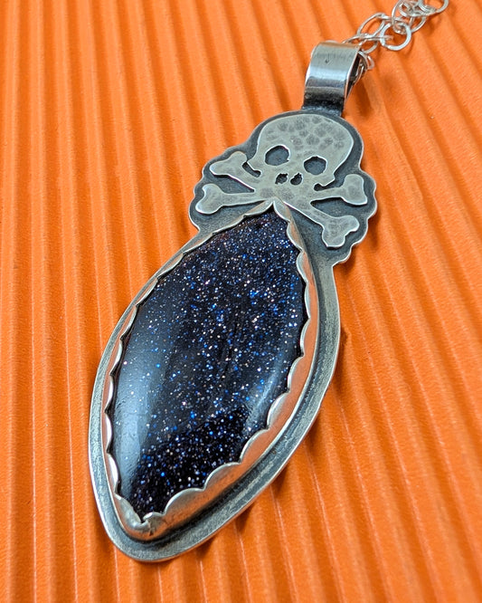 Sterling silver skull necklace with blue goldstone on orange background
