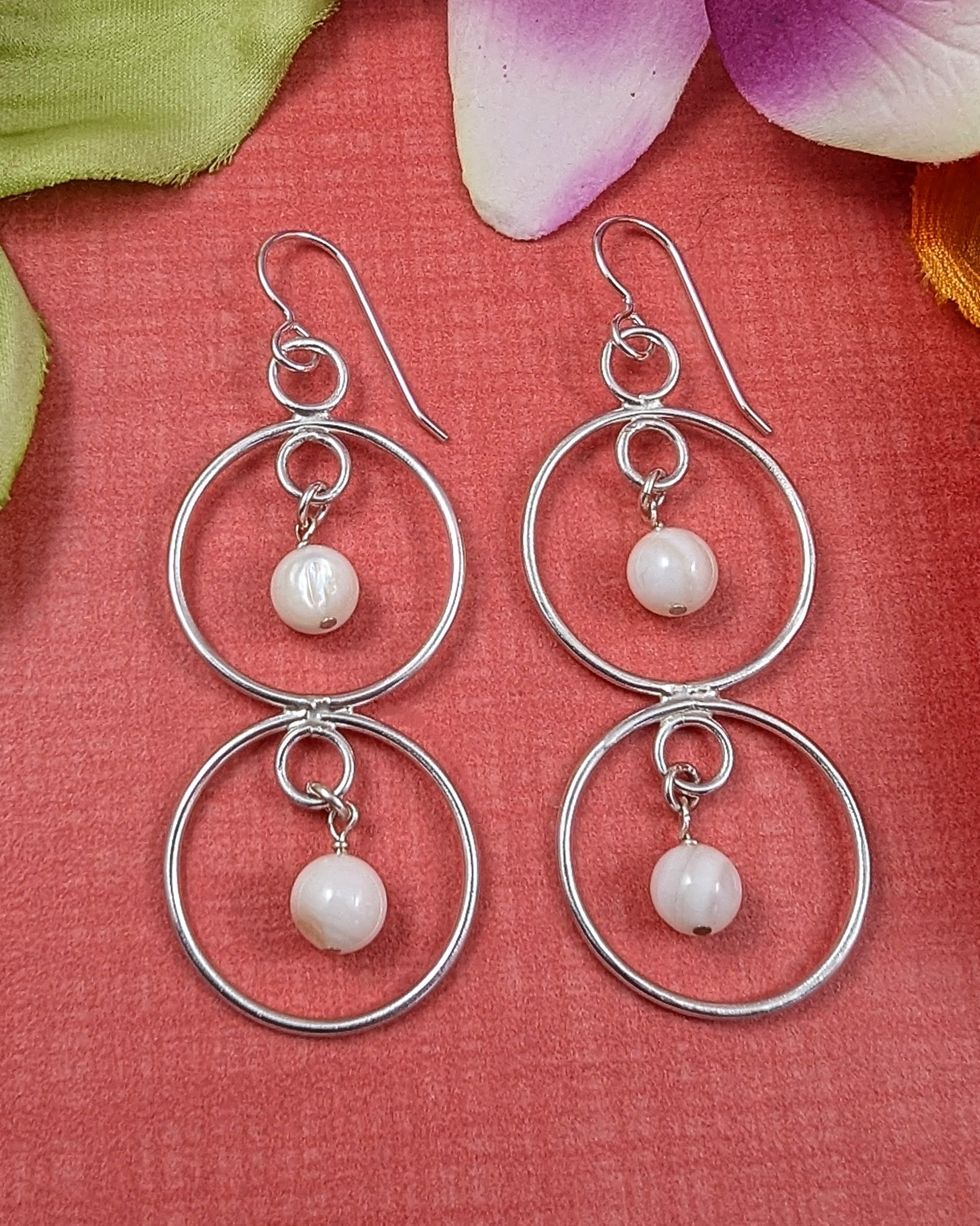 Double circle sterling silver earrings with mother of pearl beads on a coral colored background