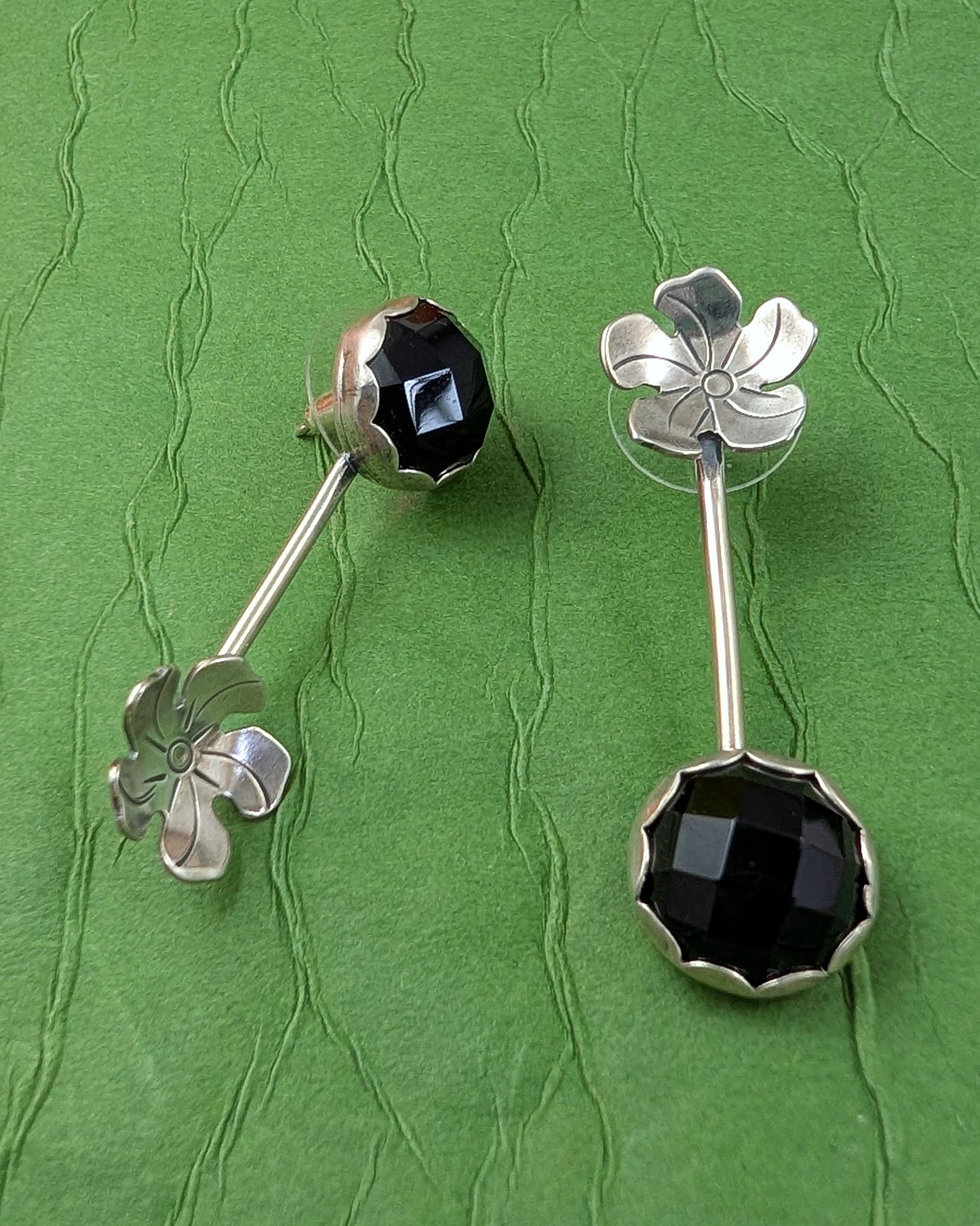 Silver earrings with onyx and flowers on a green textured background