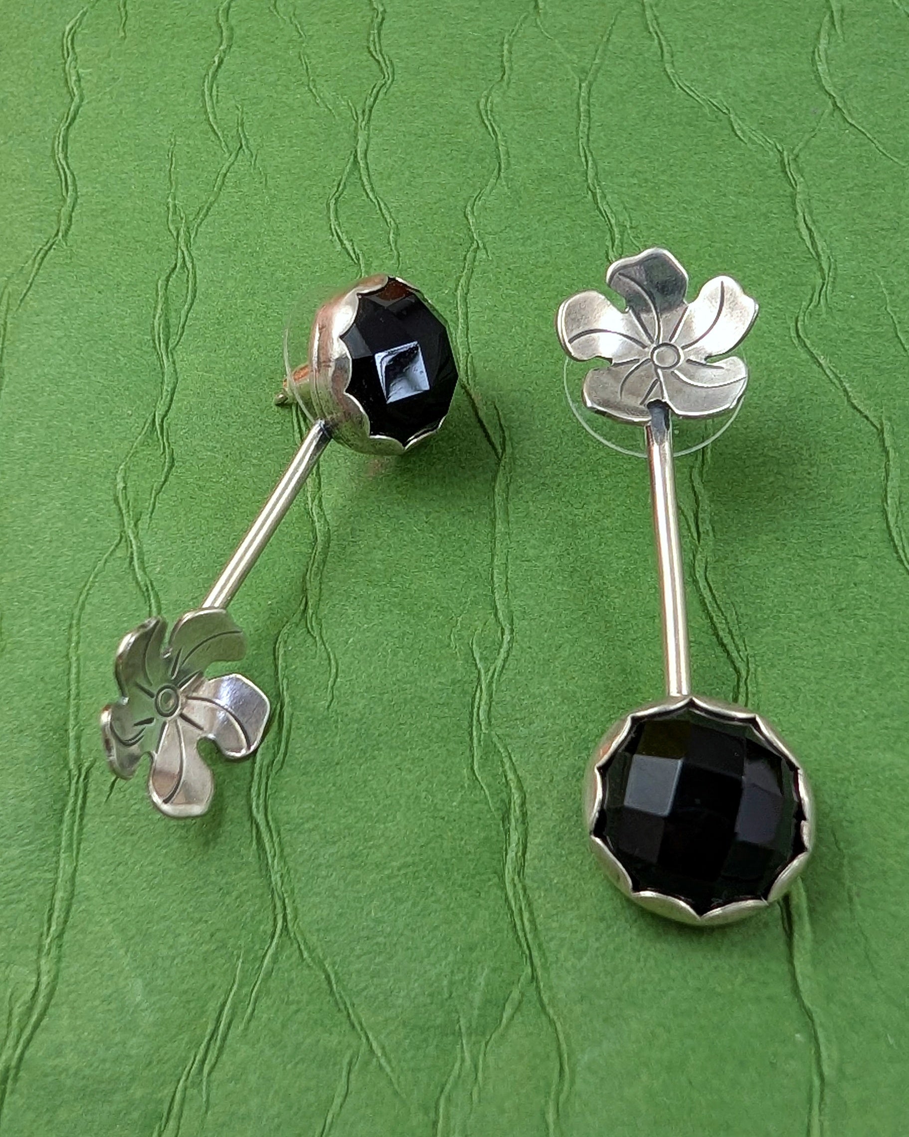 Silver earrings with onyx and flowers on a green textured background