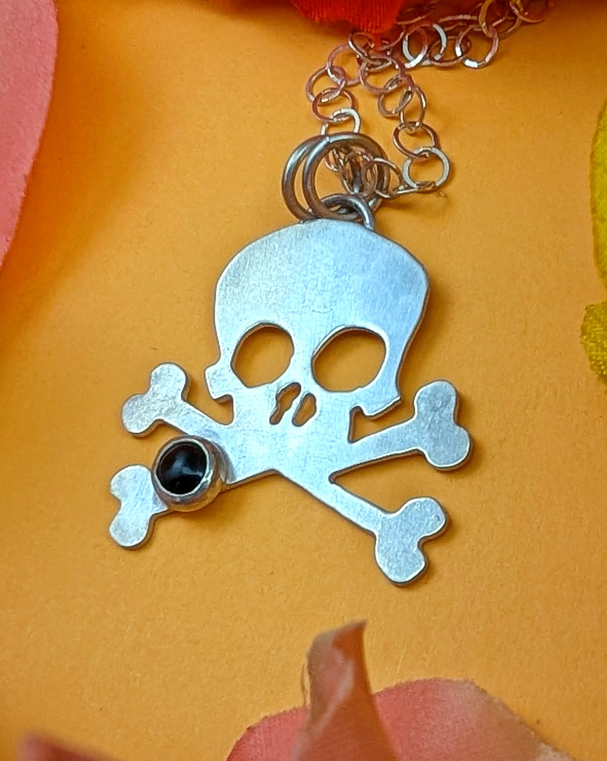 Silver skull and crossbones pendant with a black gemstone on a yellow background