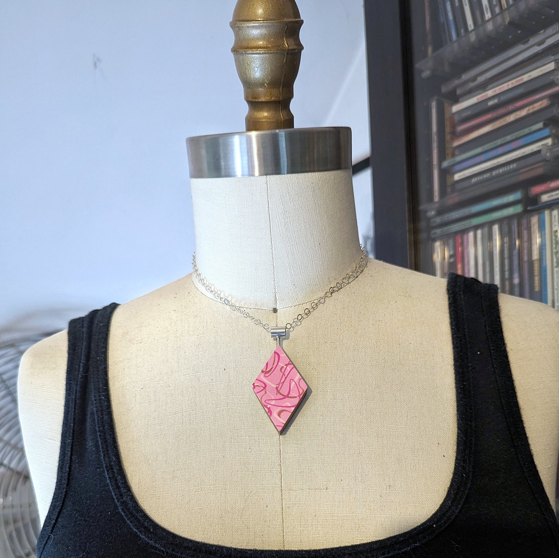 Pink boomerang laminate diamond shaped necklace with a mid century modern aesthetic on a dress form