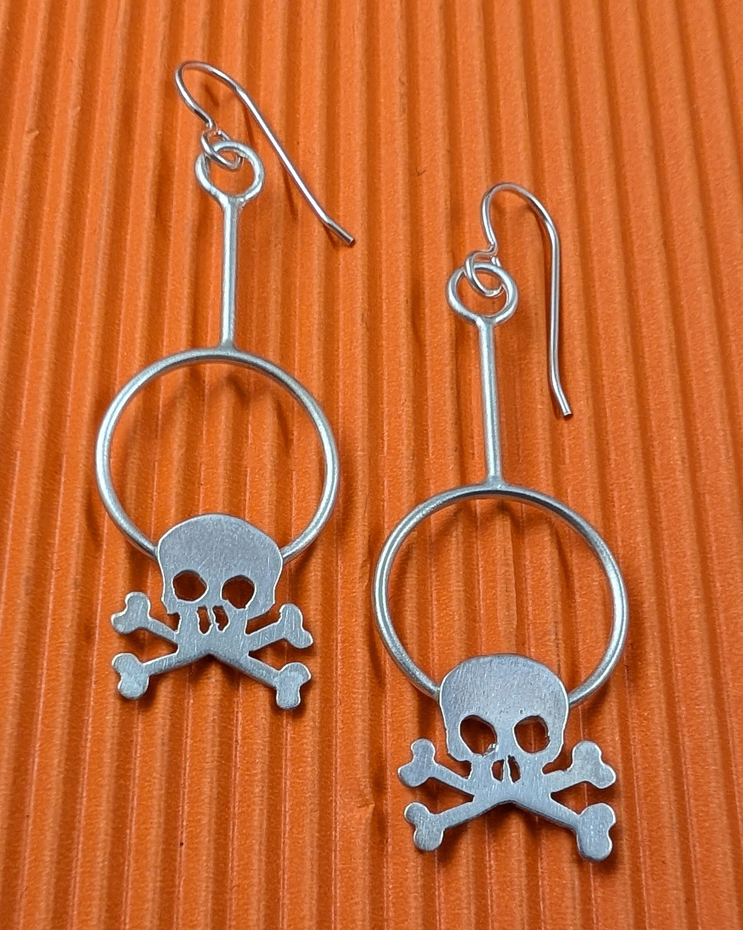 Silver skull and crossbones earrings on an orange textured background