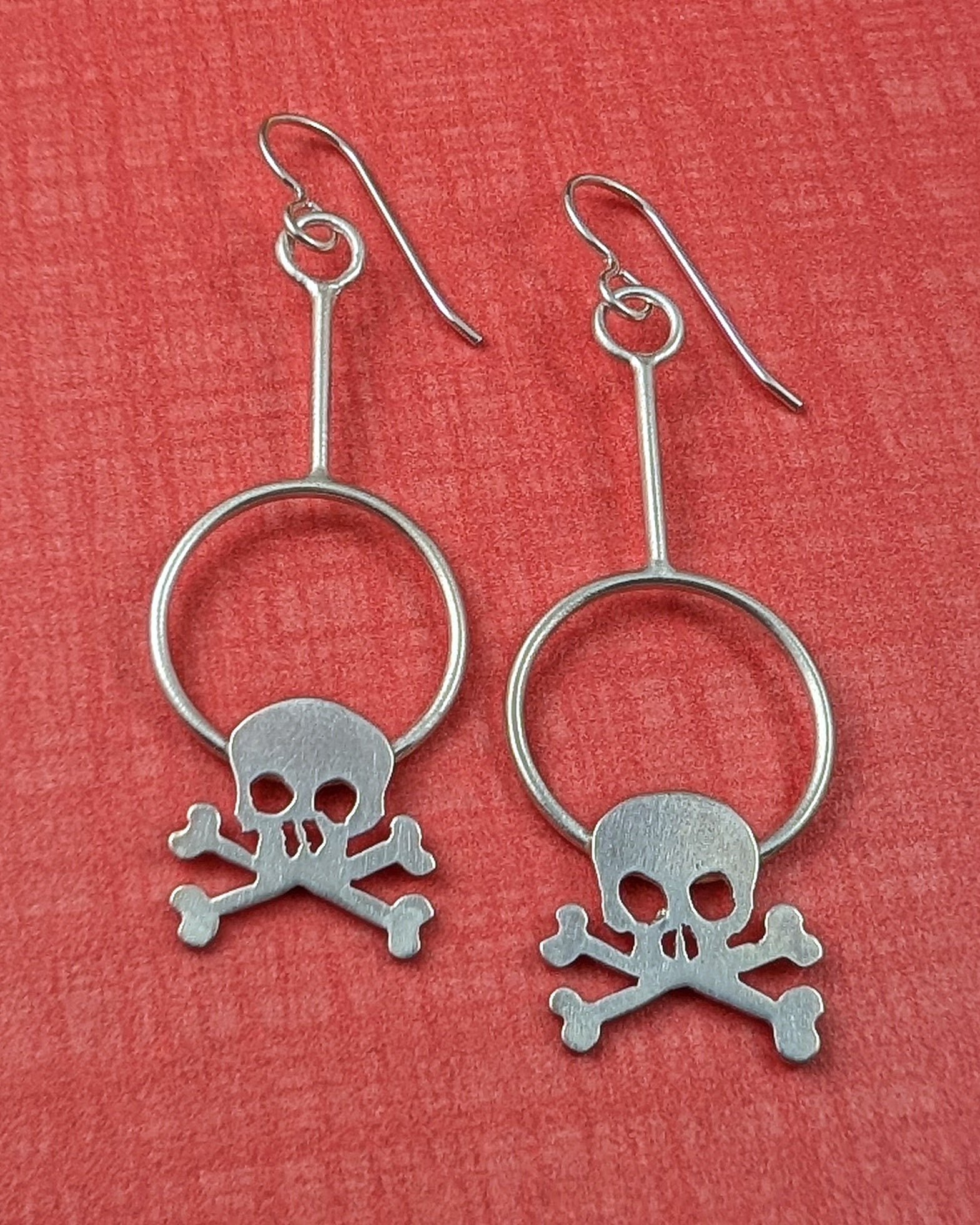 Silver skull and crossbones hoop earrings on a red background