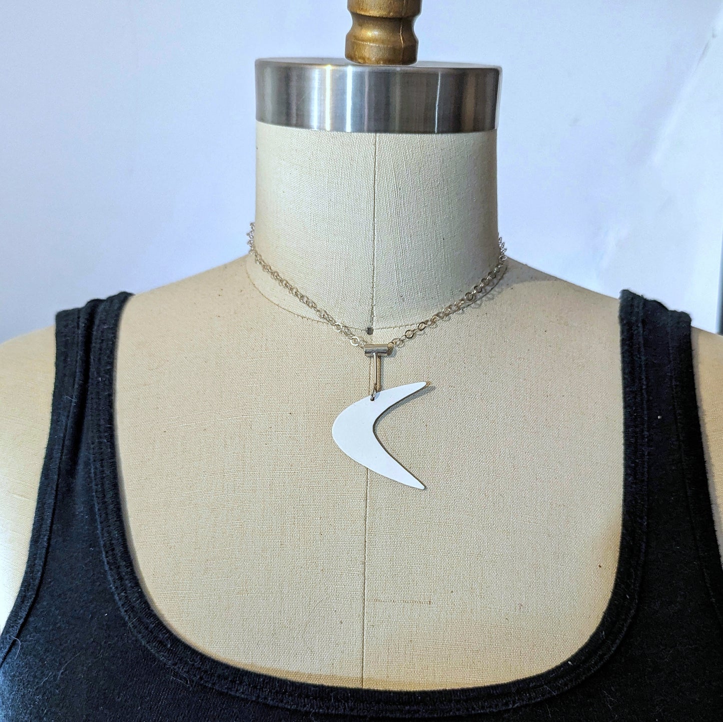 Mid century modern inspired white boomerang metal necklace on a dress form