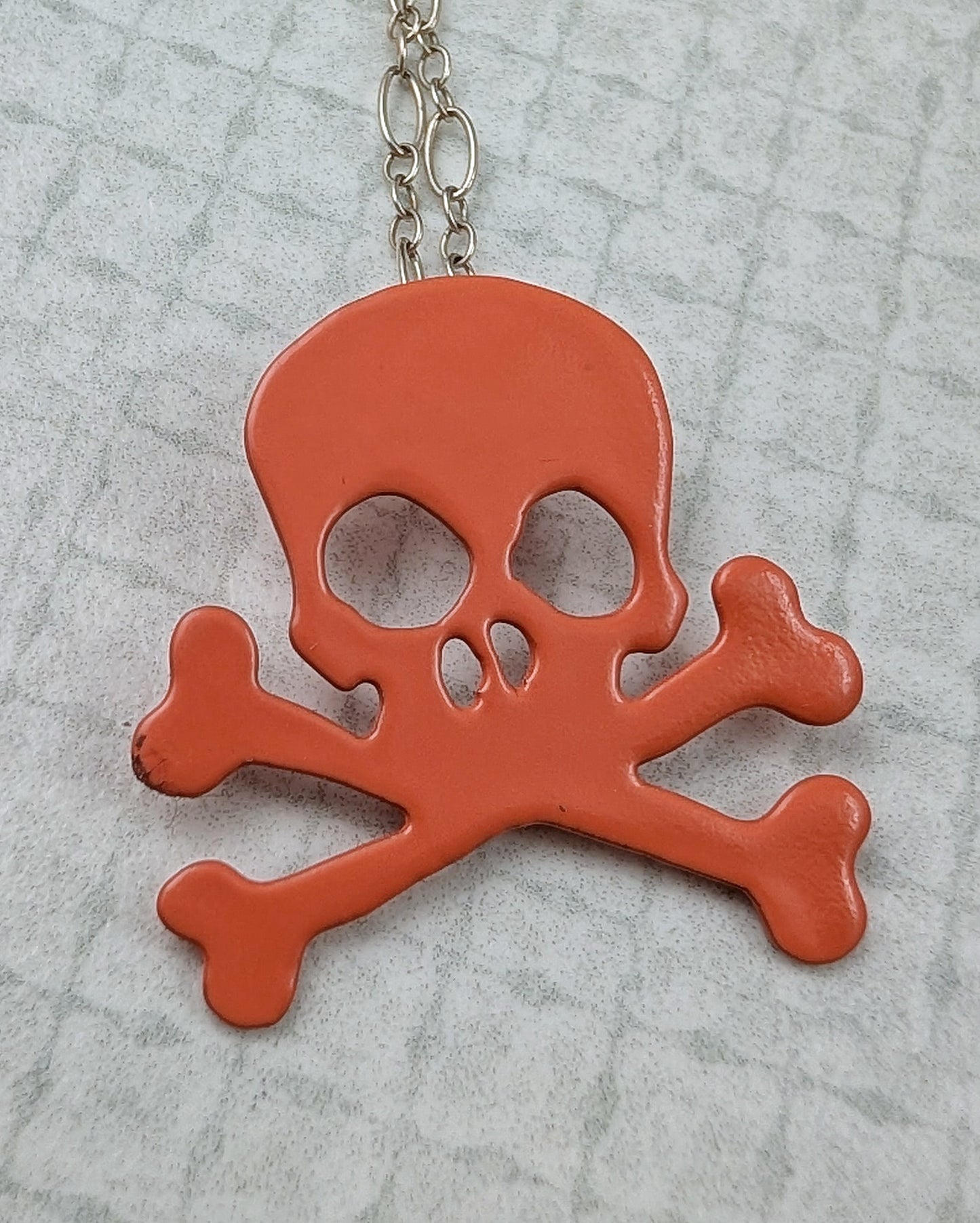Orange skull and crossbones pendant on a chain against a gray textured background