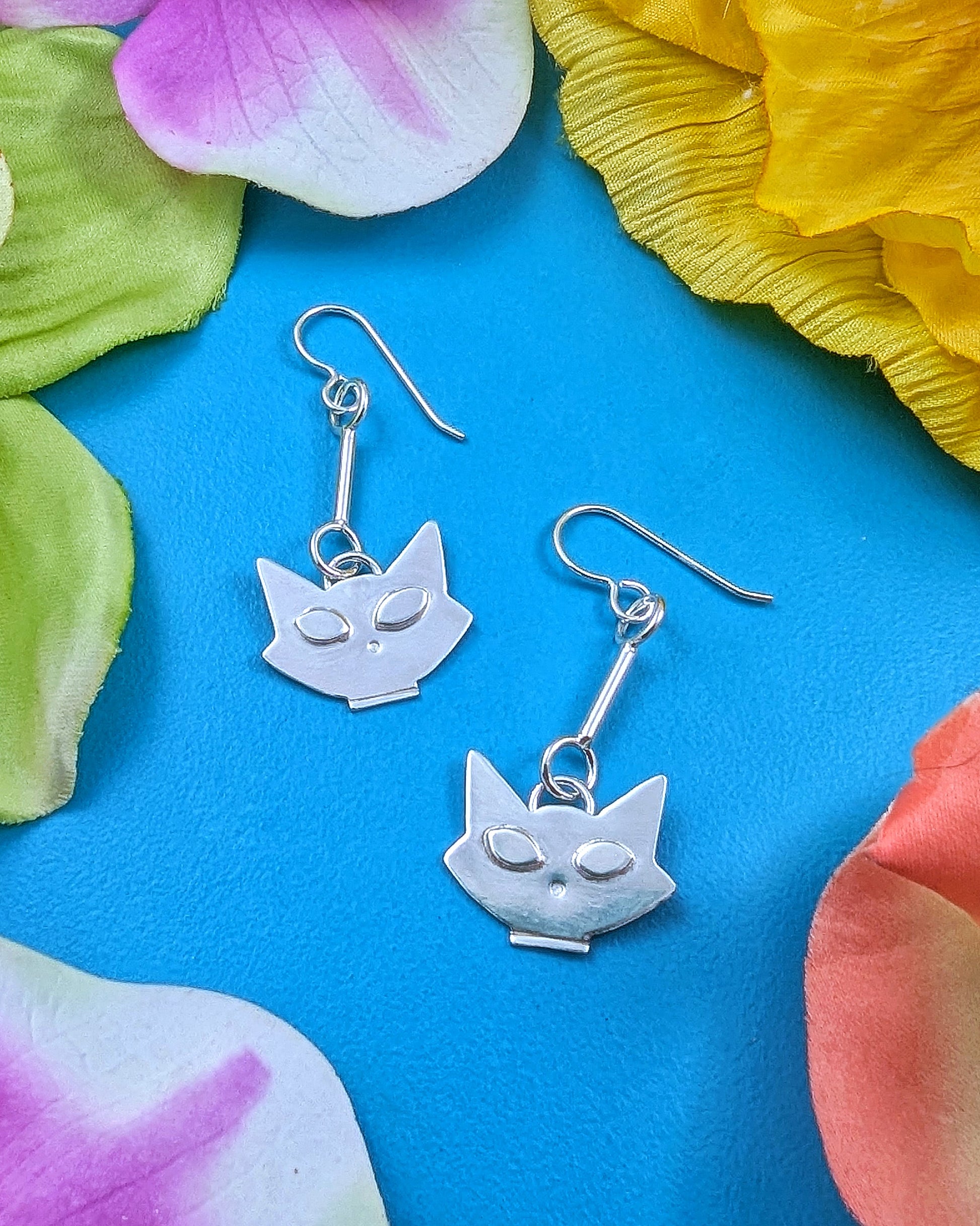 Mid century modern inspired kitty cat earrings on a turquoise background with flowers