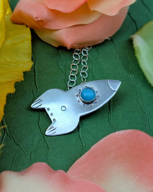 Sterling silver rocket ship necklace on a green backgroud