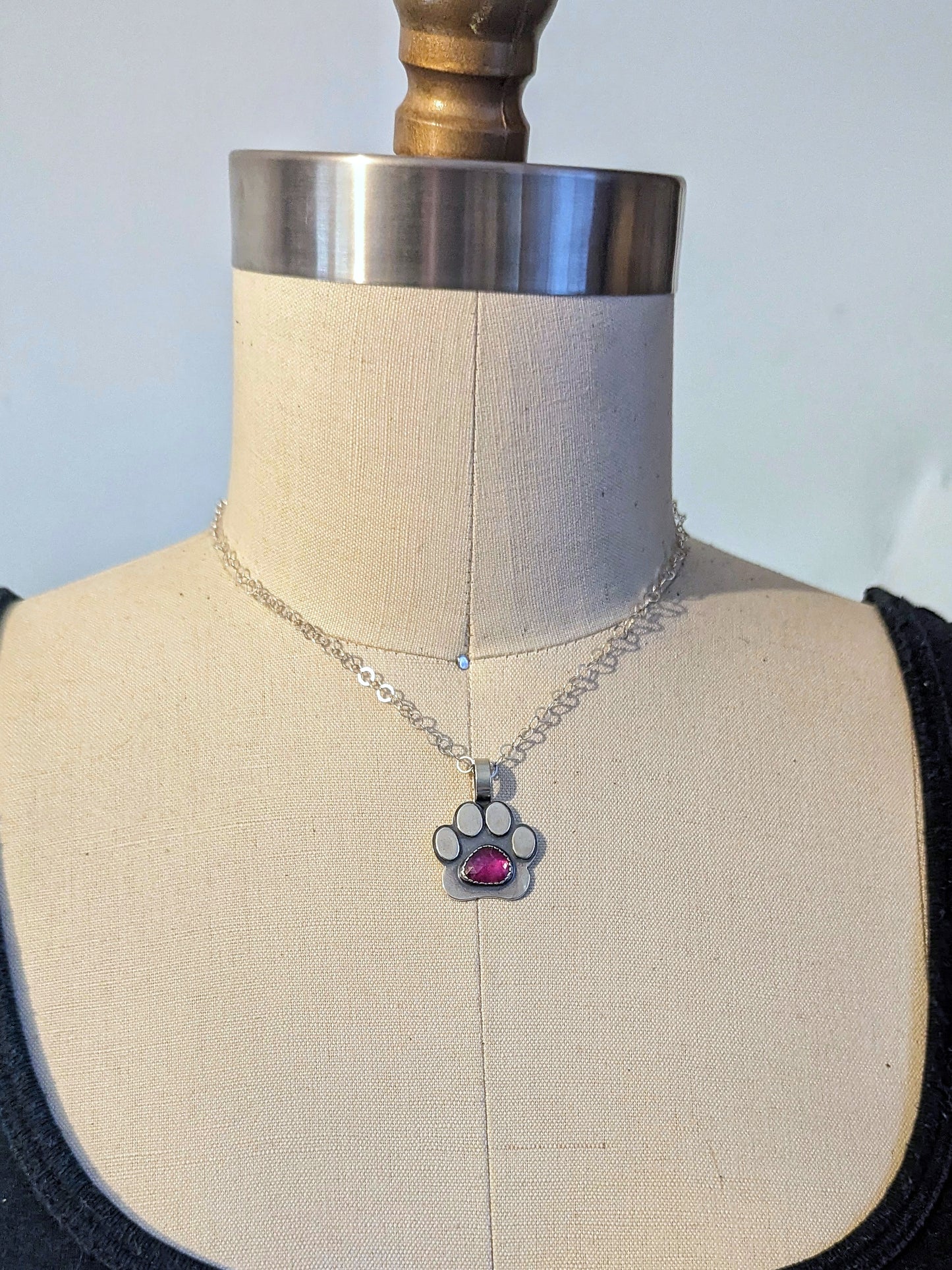 Sterling silver paw print necklace with ruby shown on a dress form