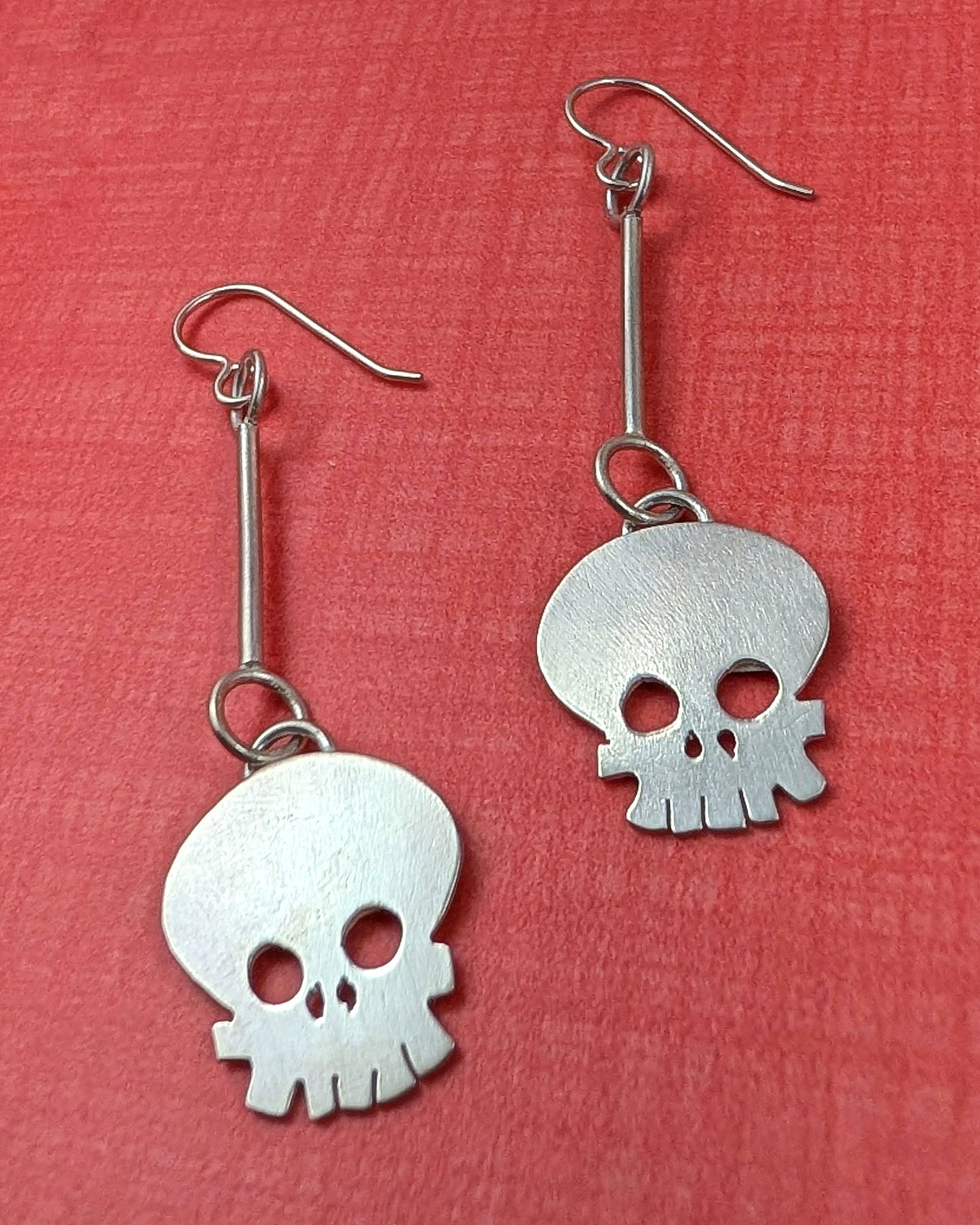 Witch Doctor sterling silver skull earrings on an orange background
