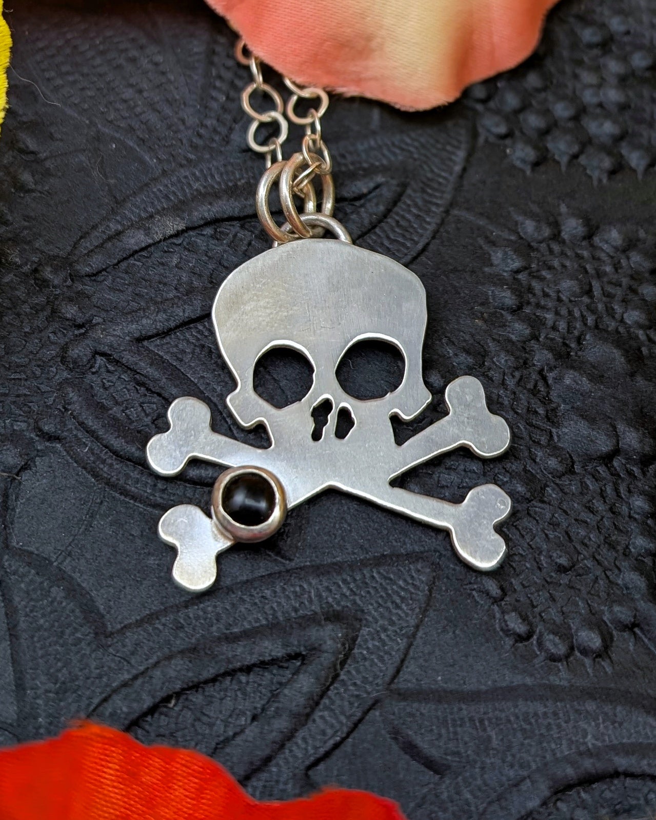 Silver skull and crossbones pendant with onyx on a dark textured background