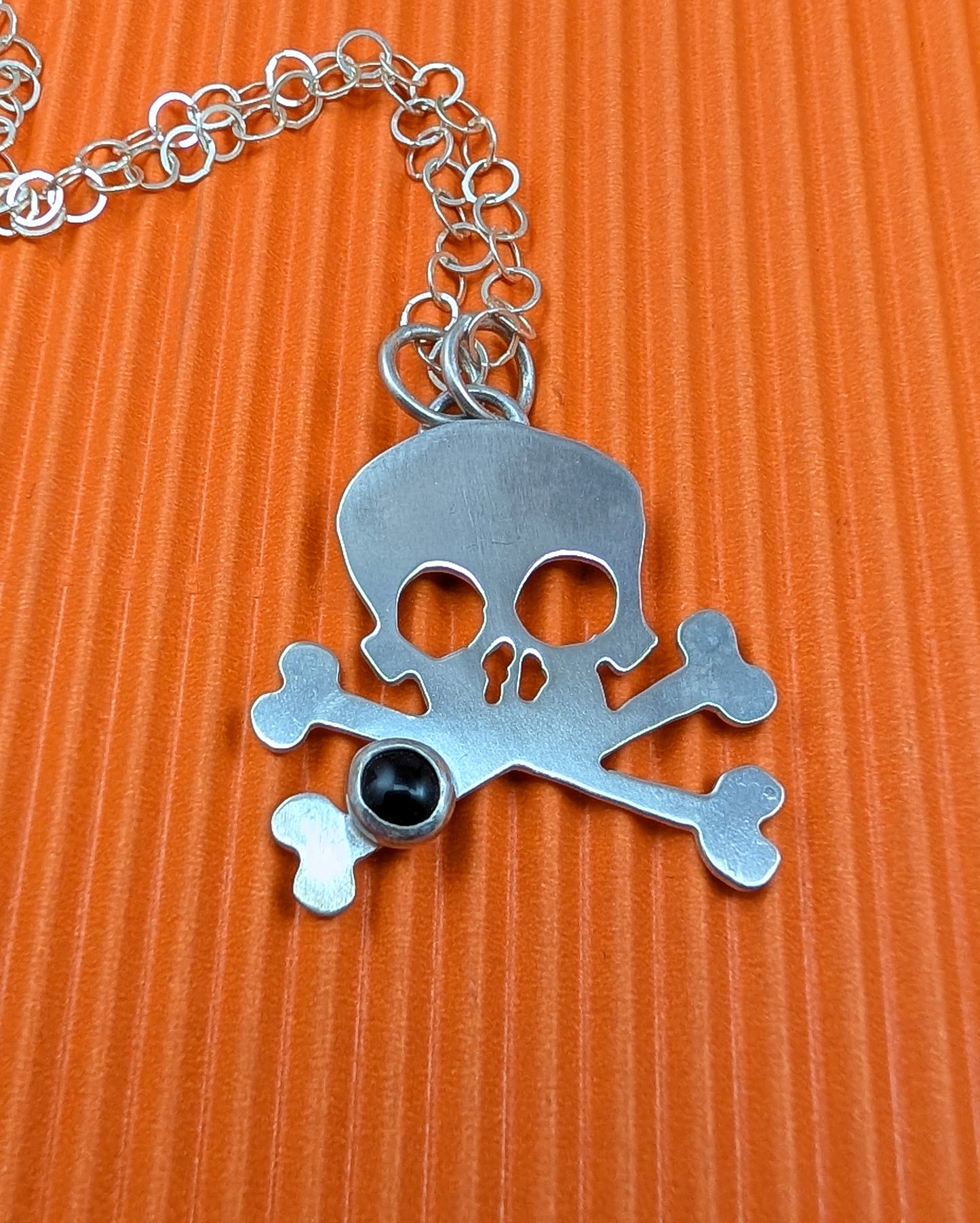 Skull and crossbones pendant with a black gemstone on an orange background
