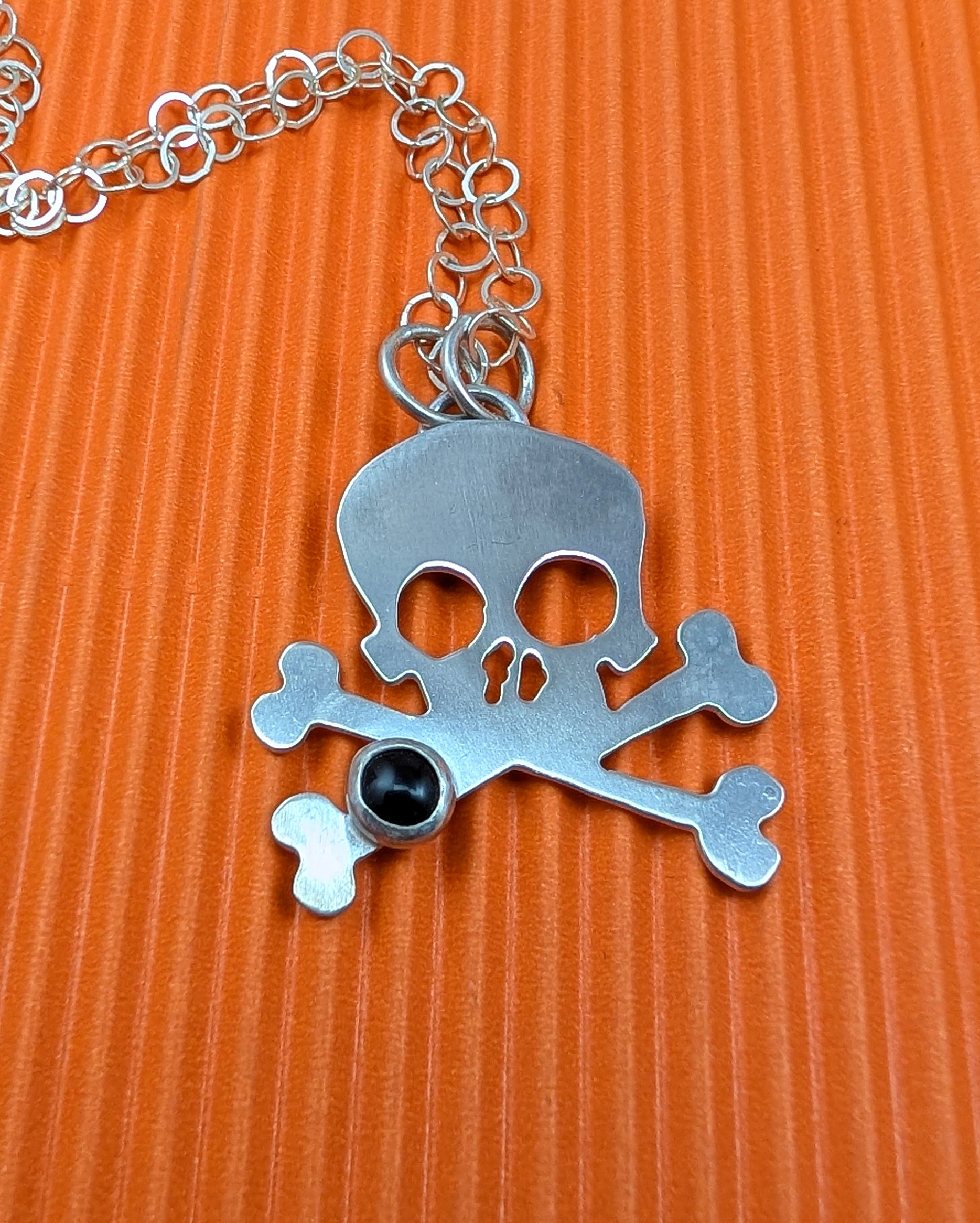 Skull and crossbones pendant with a black gemstone on an orange background