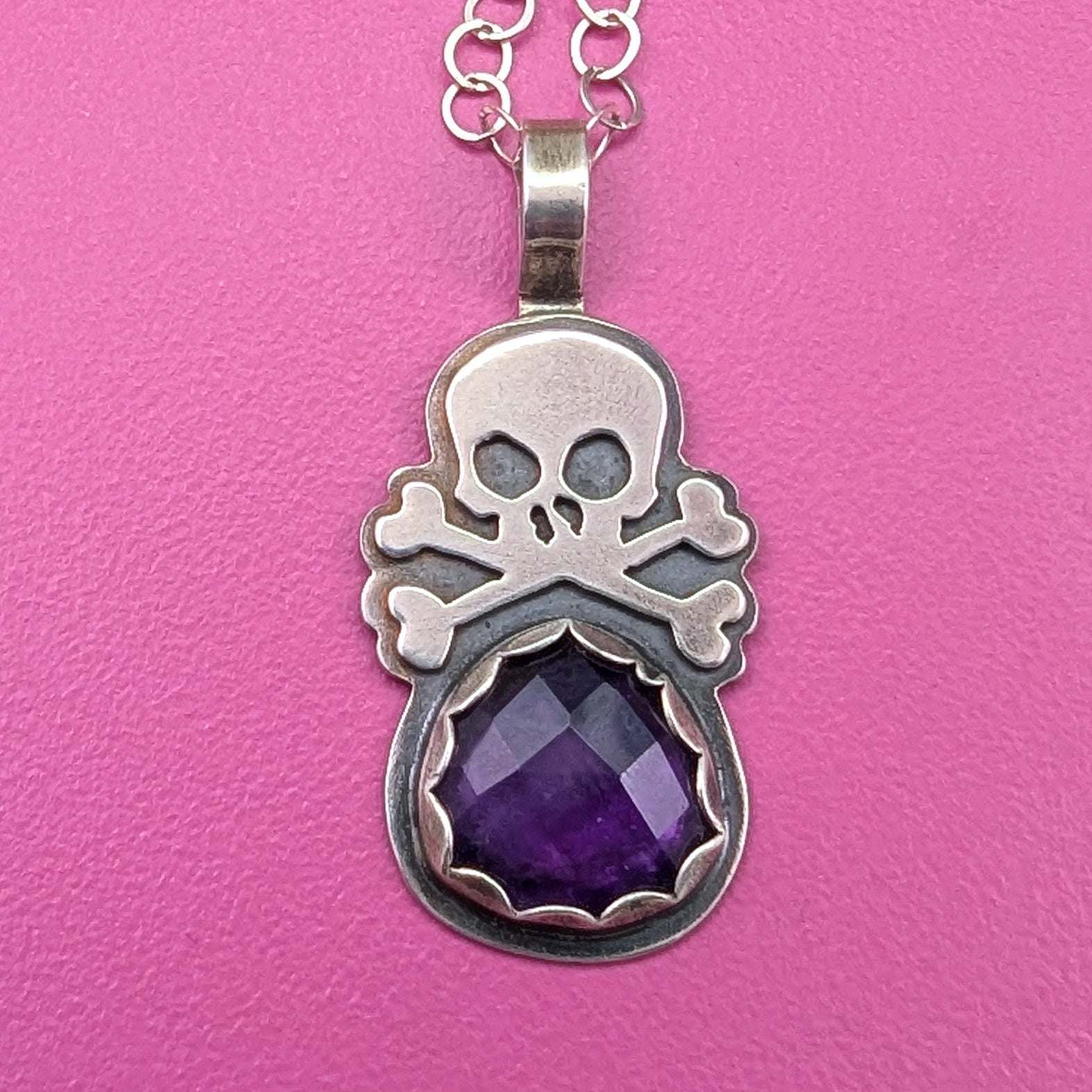 Sterling silver skull necklace with a  purple rosecut amethyst shown on a pink background