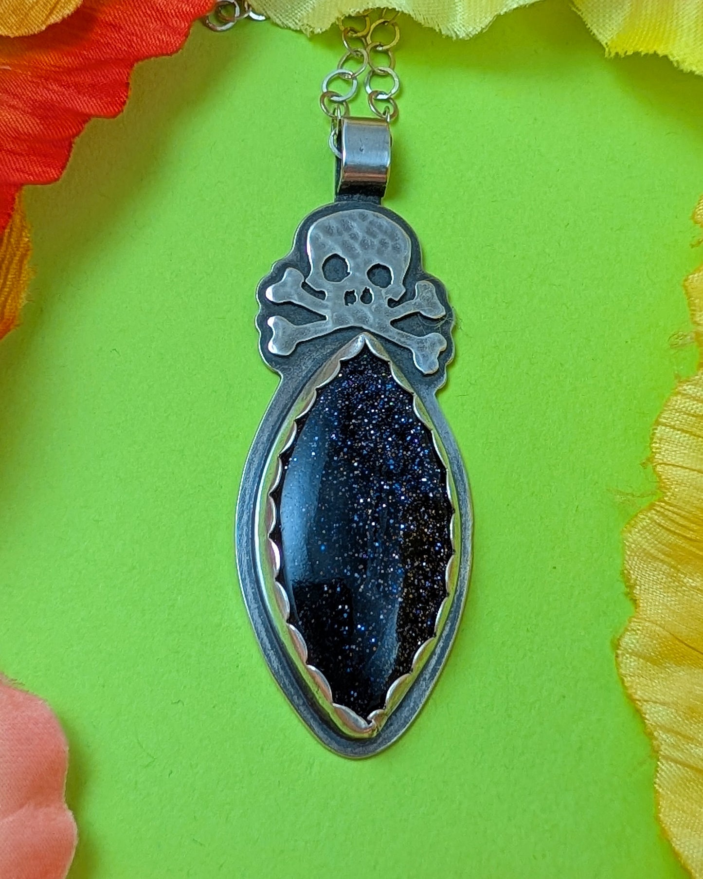 Sterling silver skull necklace with blue goldstone on green background