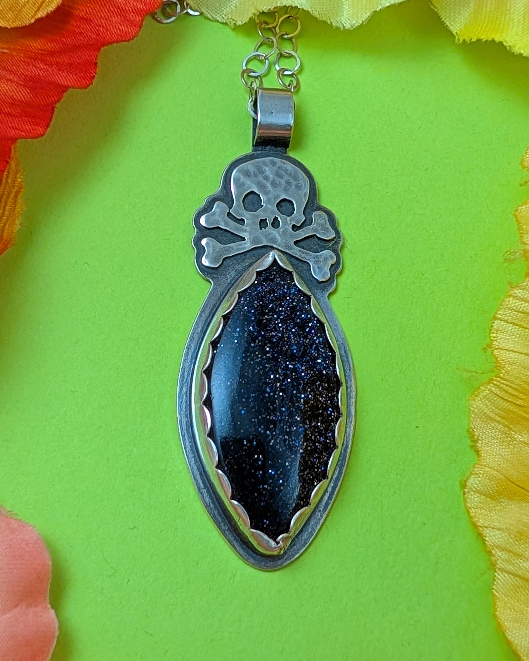 Sterling silver skull necklace with blue goldstone on green background