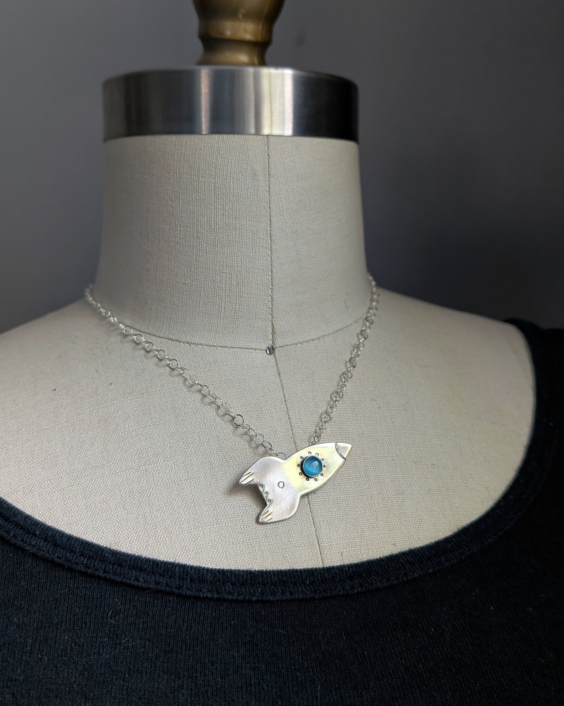 Necklace with a rocket ship on a mannequin against a dark background