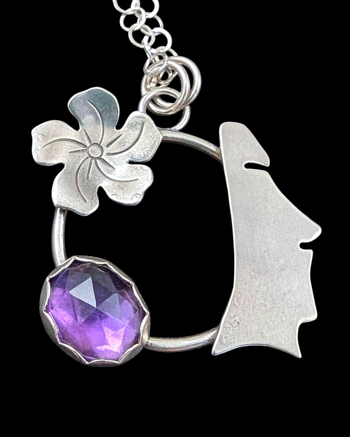 Sterling silver moai head necklace with amethyst on black background.