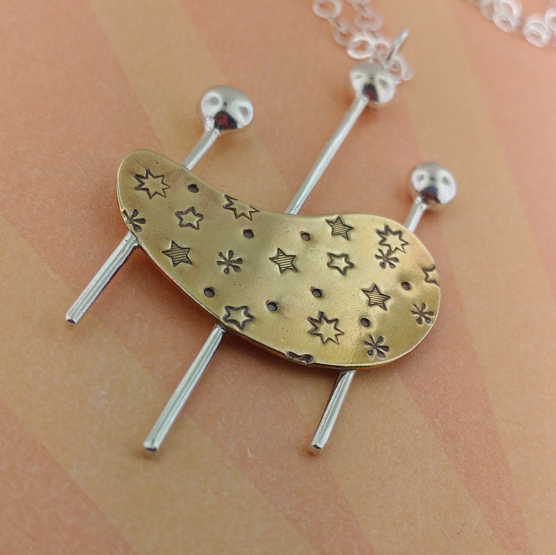 Mid century modern jewelry featuring a brass kidney shape with sterling silver rods