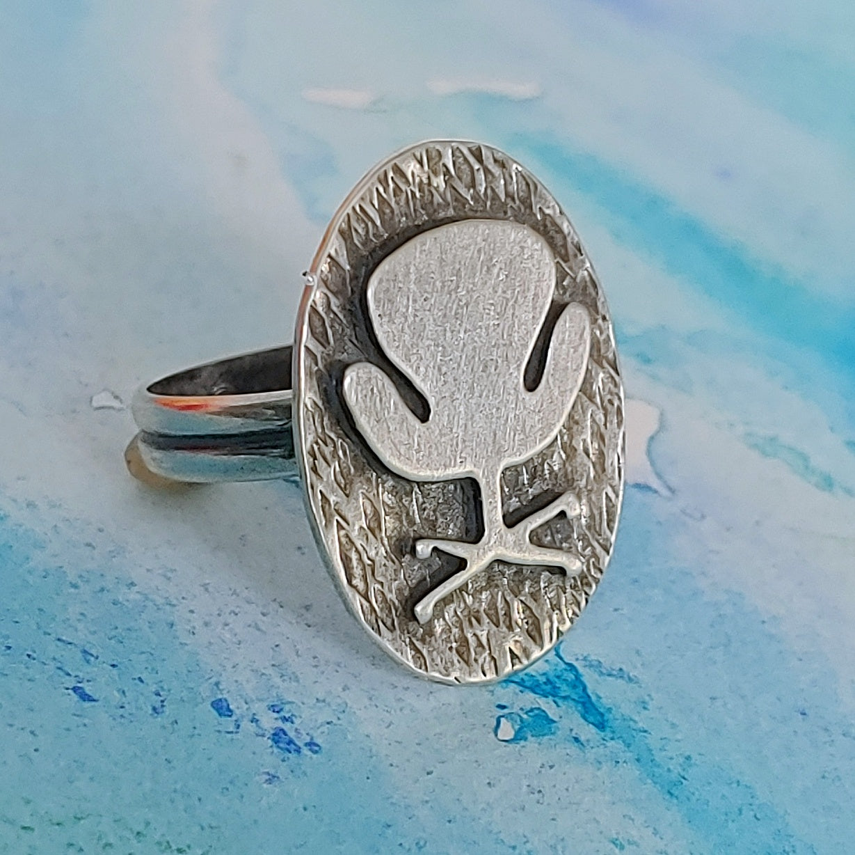 Mid century modern Swan Chair ring handmade in sterling silver which is perfect as a 17th wedding anniversary gift of furniture as shown on a blue background