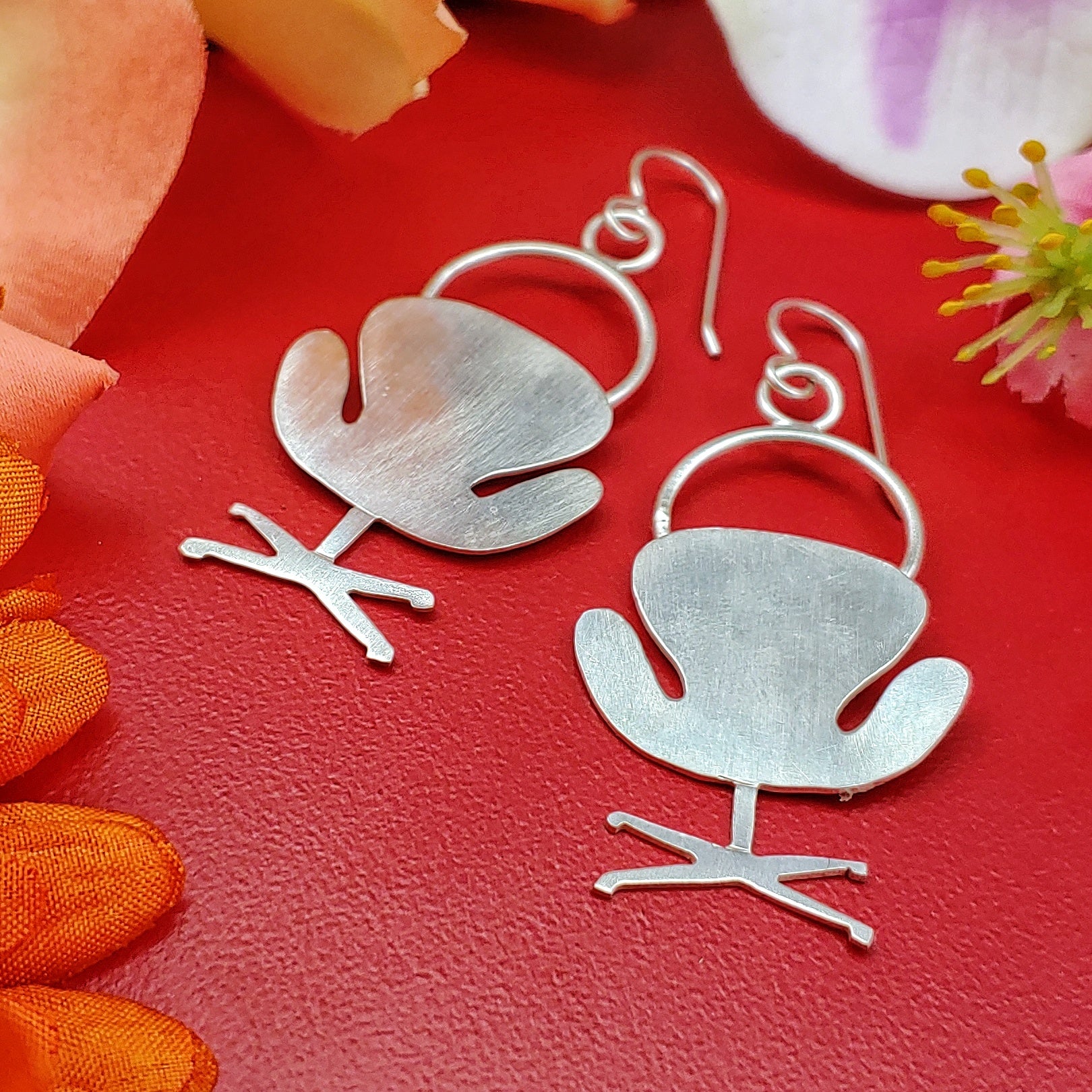 Mid century modern swan chair earrings handmade in sterling silver which are perfect for the 17th wedding anniversary gift of furniture as shown on a red background with flowers