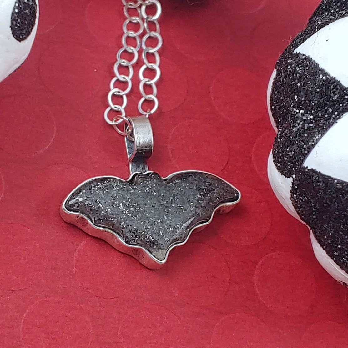 Midnight quartzite bat necklace on a red background with black and white pumpkins.
