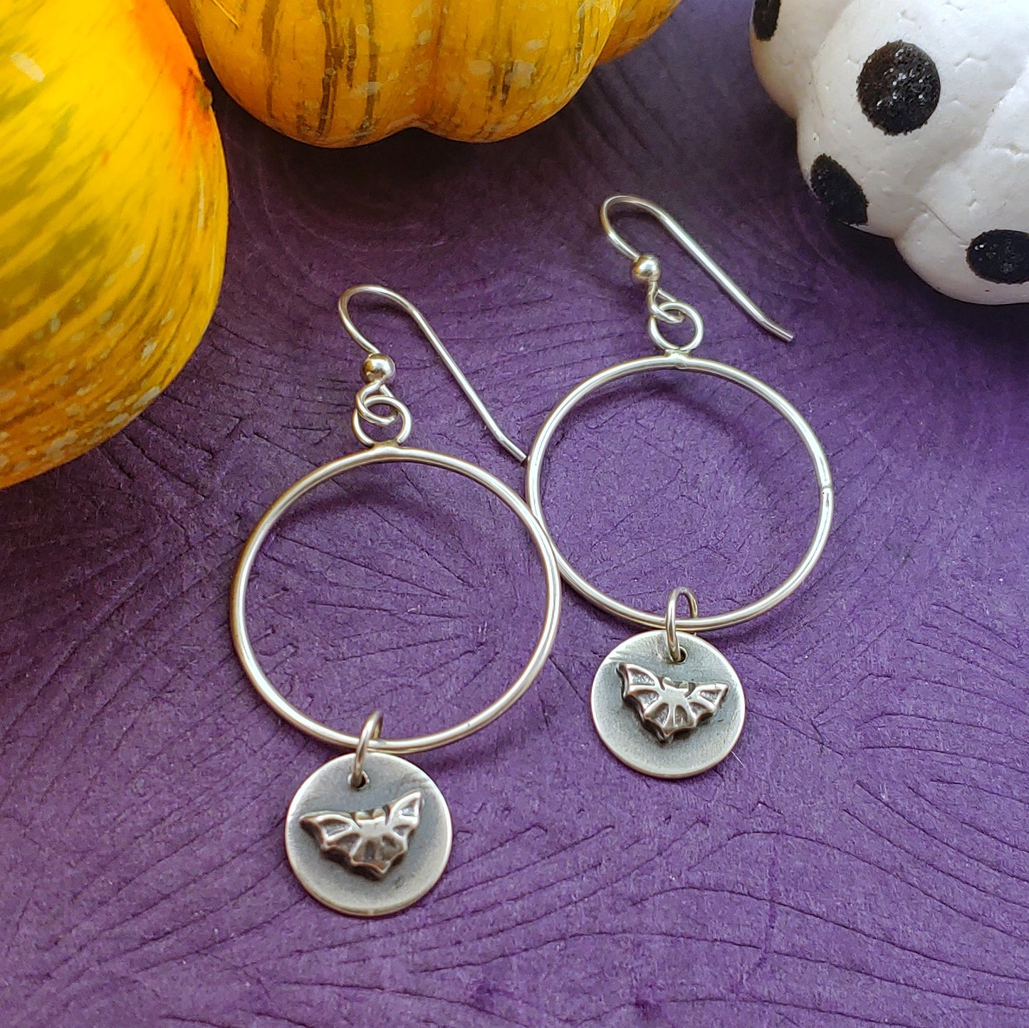 Sterling silver hoops with bat dangles on a purple background with little colorful pumpkins surrounding it.