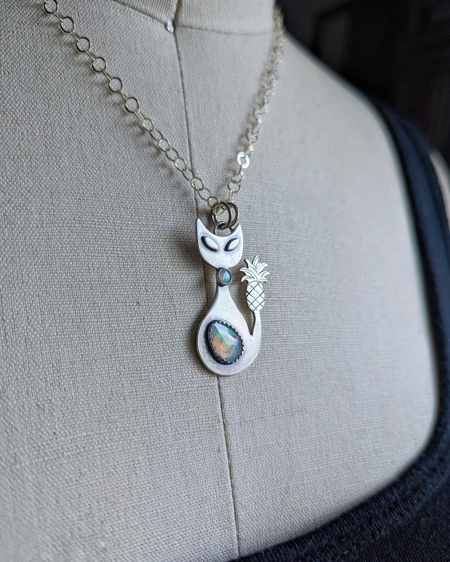 Sterling silver handmade cat with pineapple tail and Ethiopian opal on a dress form side view