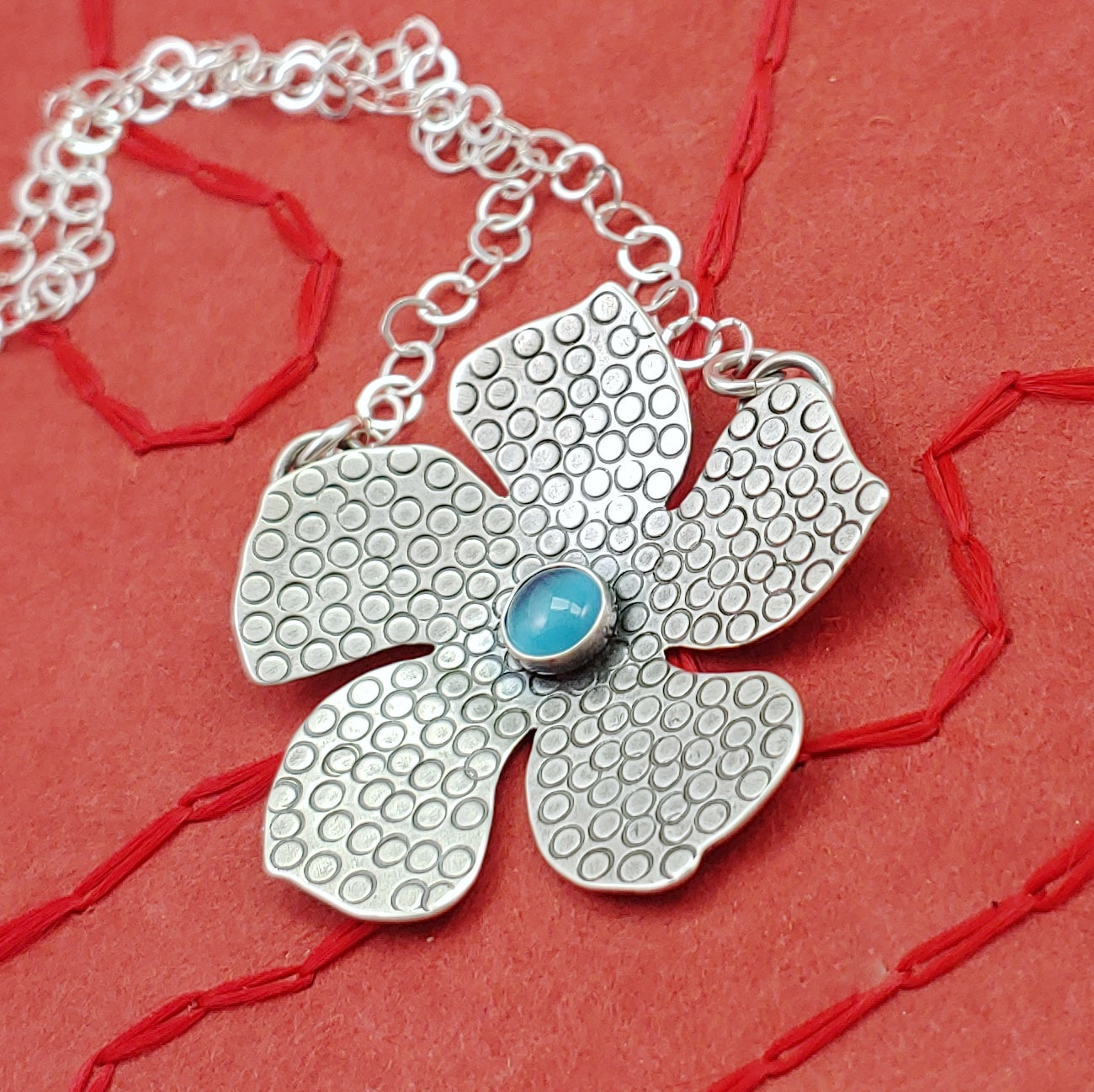 Handmade sterling silver flower necklace with stamped details and a light blue cats eye stone