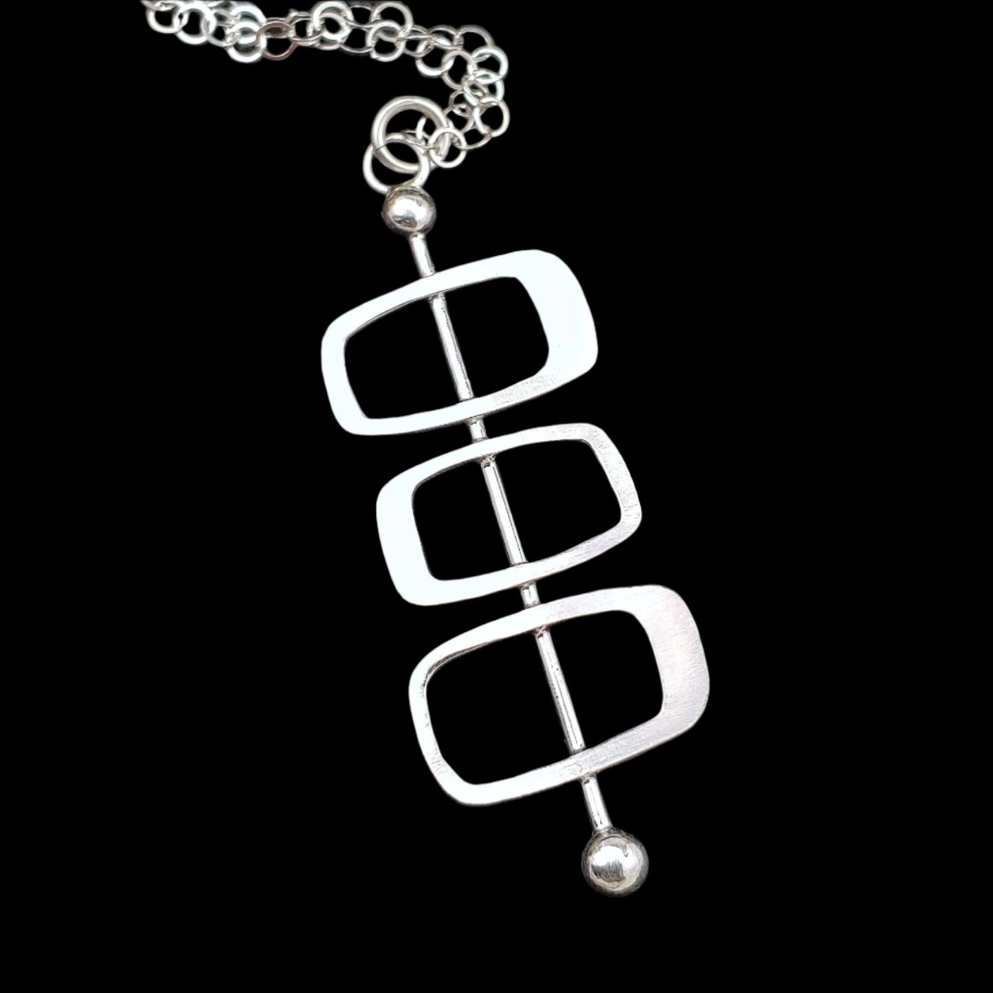Handmade sterling silver modernist necklace featuring Googie inspired architectural soft rectangles on a plain back background