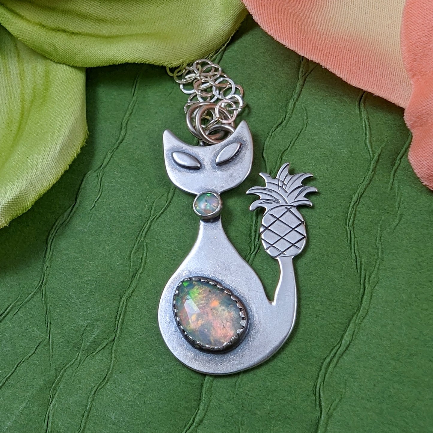 Sterling silver handmade cat with pineapple tail and Ethiopian opal on green background with flowers