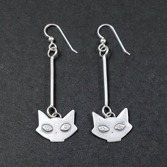Sterling silver mid century modern cat head dangle earrings on a black background.