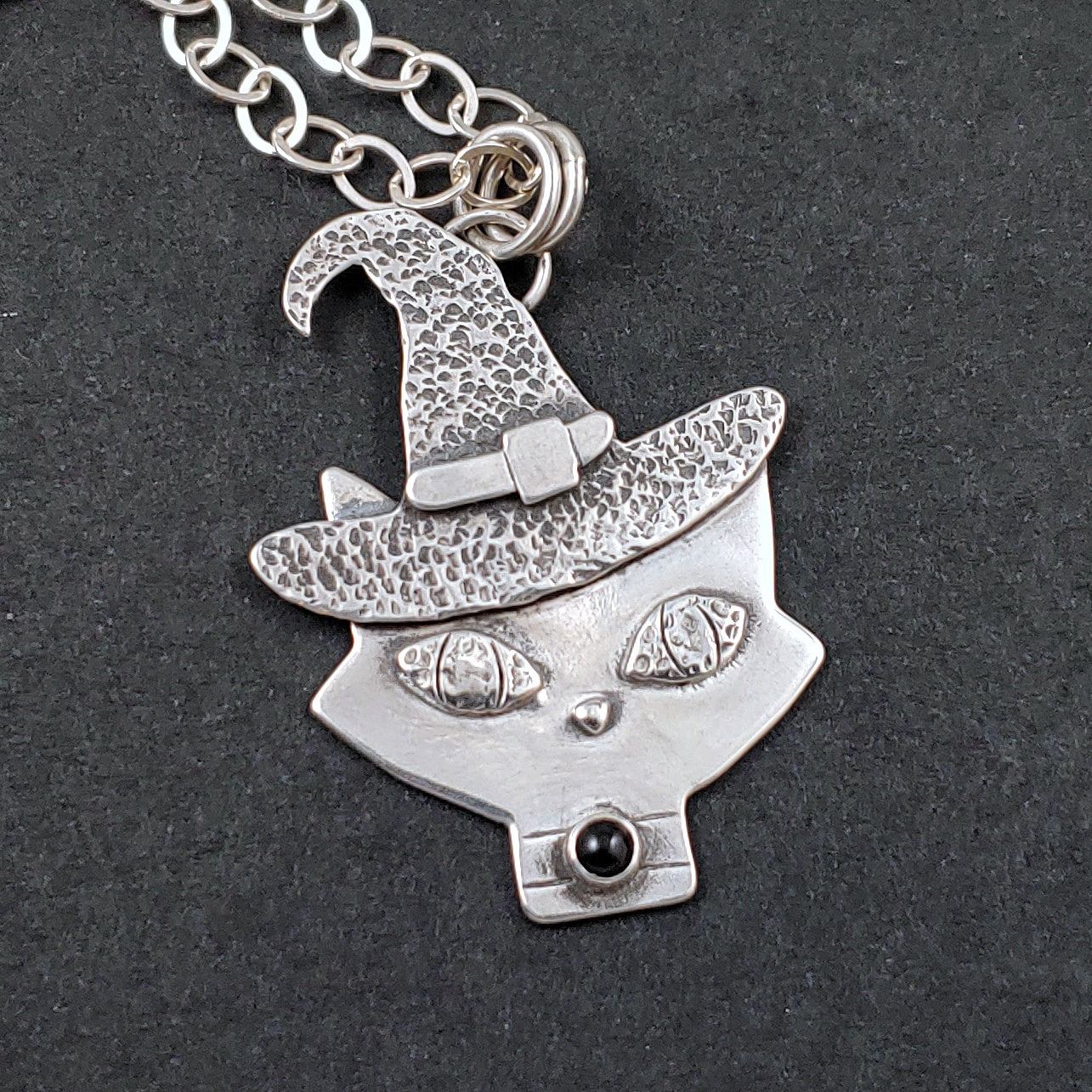 Sterling silver mid mod kitty head with textured witch hat on black background.