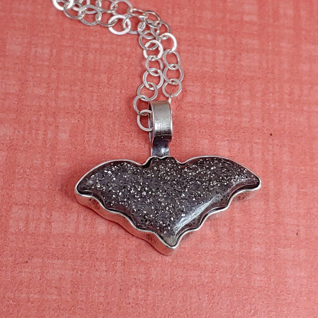 Midnight quartzite bat necklace on an orange background.