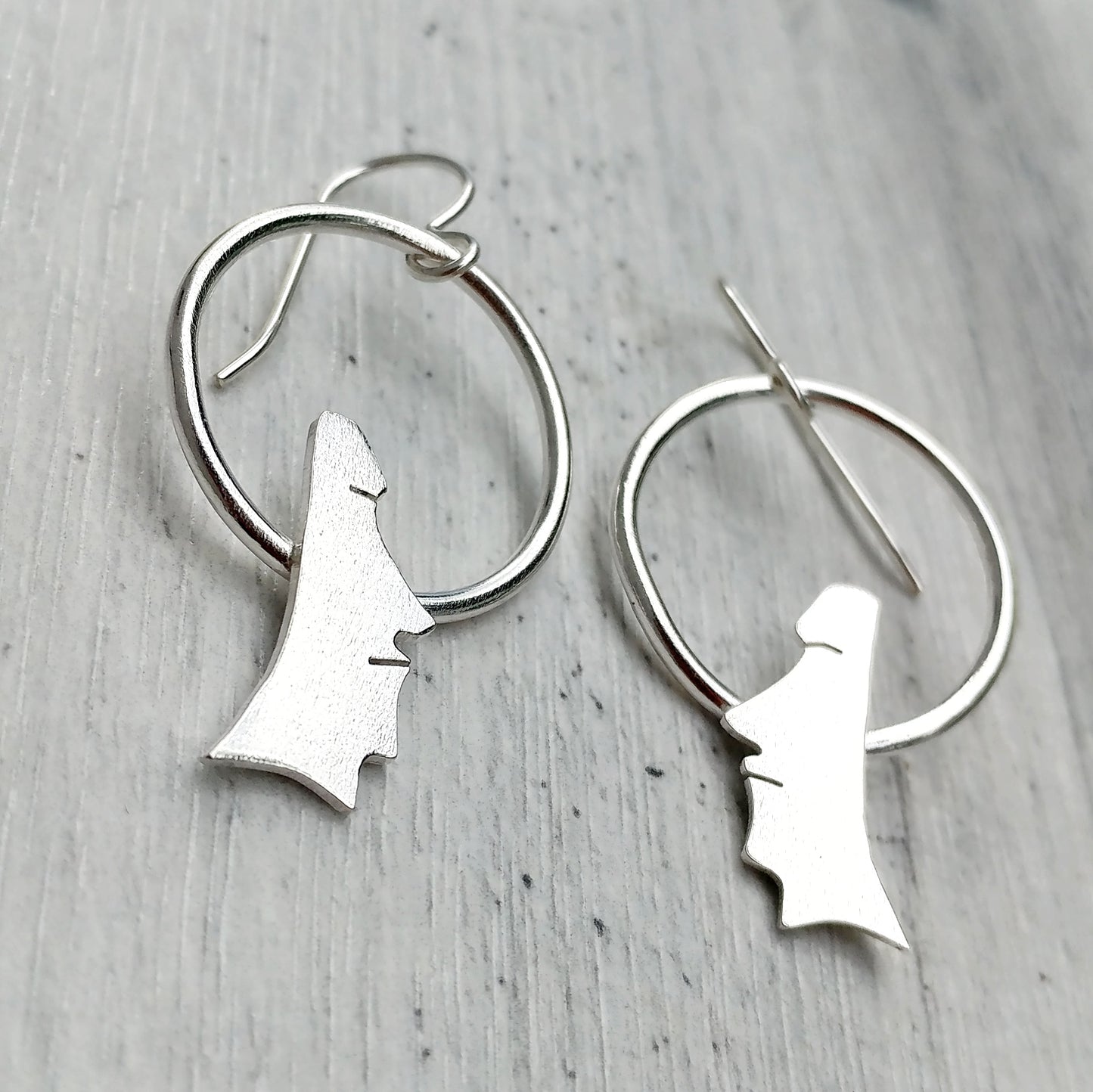 Handmade sterling silver moai head earrings on circles on a grey background.