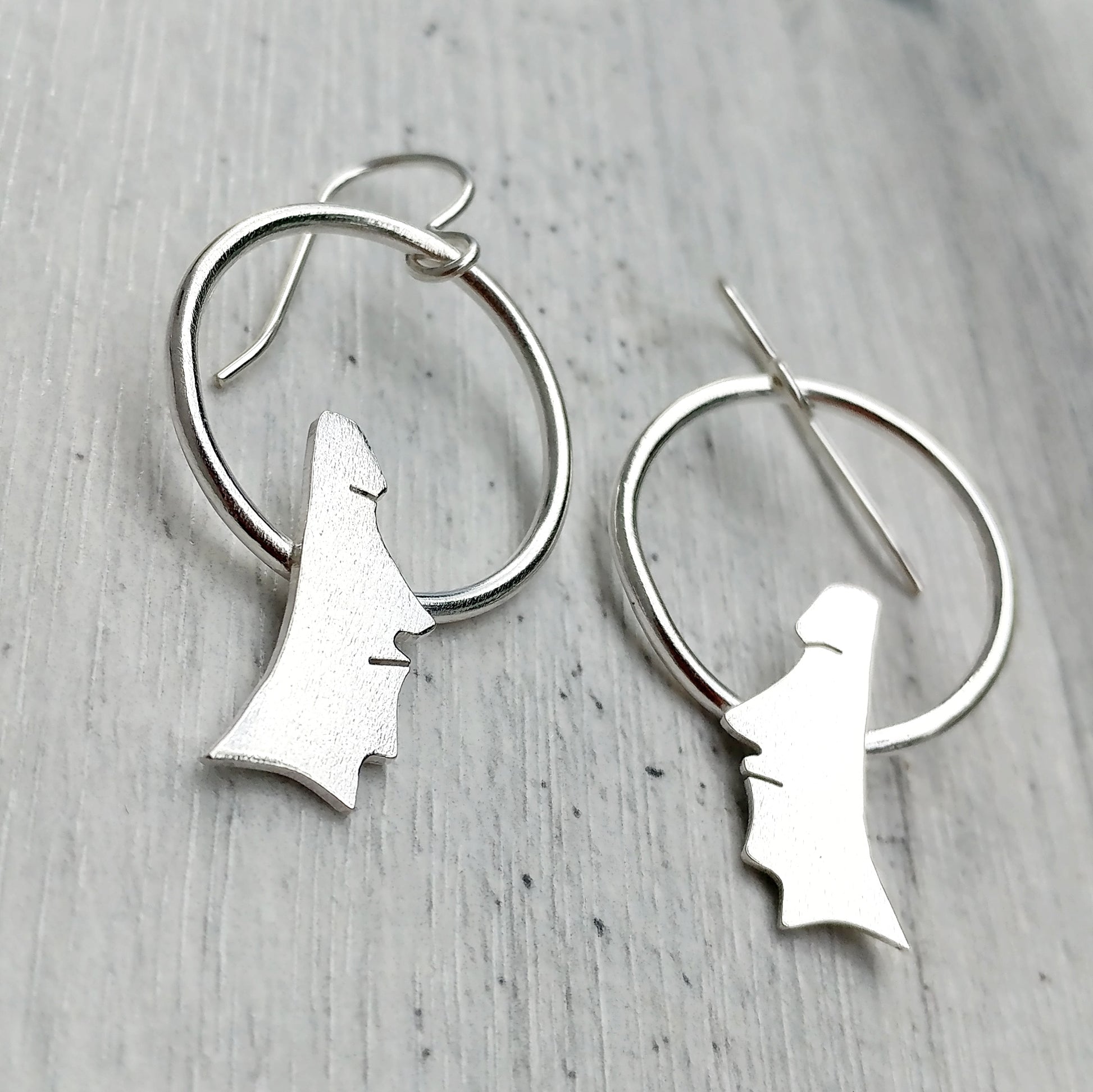 Handmade sterling silver moai head earrings on circles on a grey background.