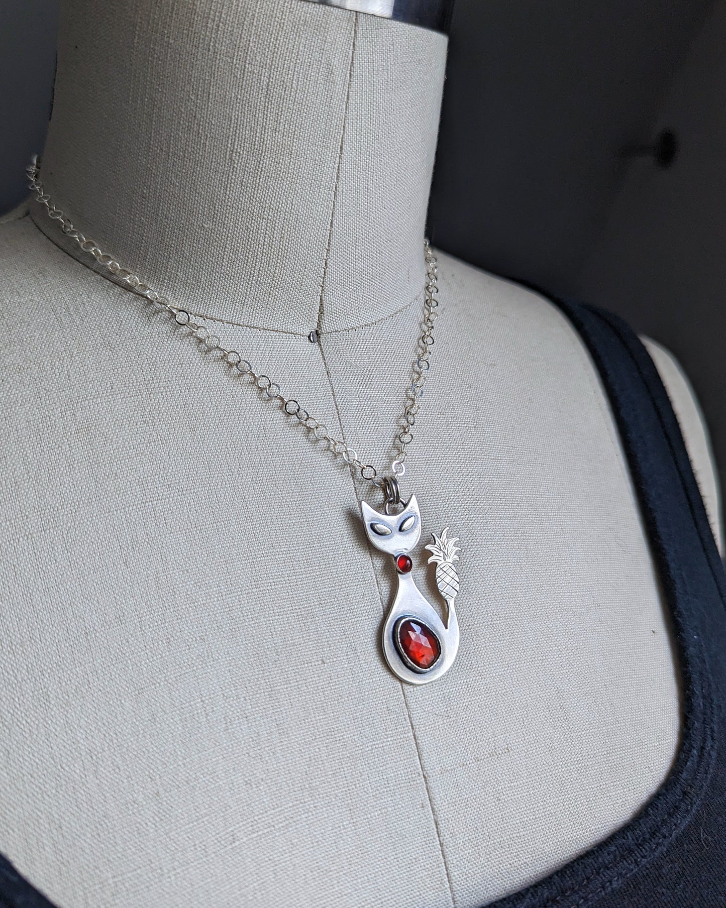 Sterling silver handmade cat with pineapple tail and garnet on a dress form to show size