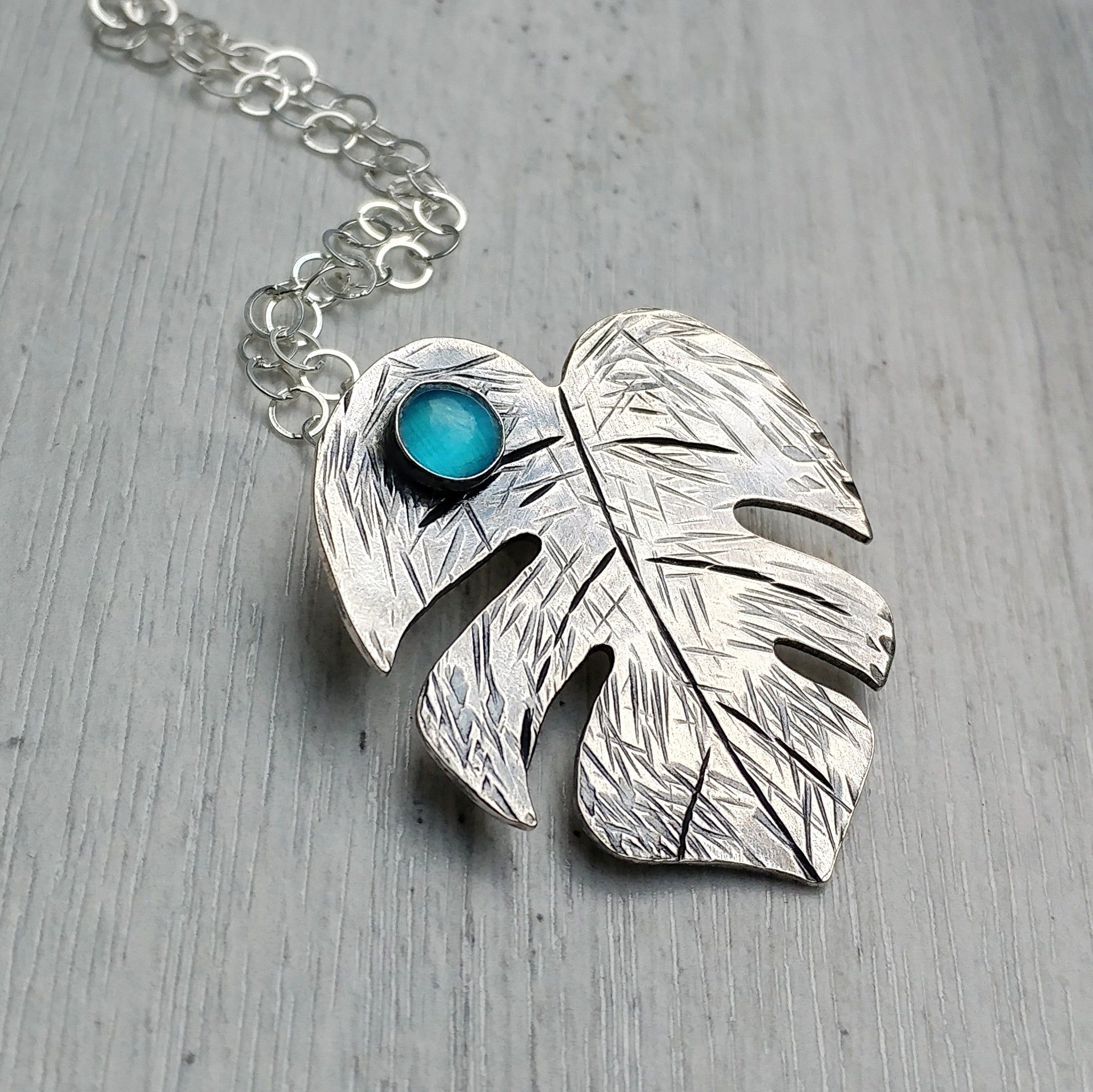 Sterling silver monstera leaf Tiki necklace featuring various gemstones shown on a gray background