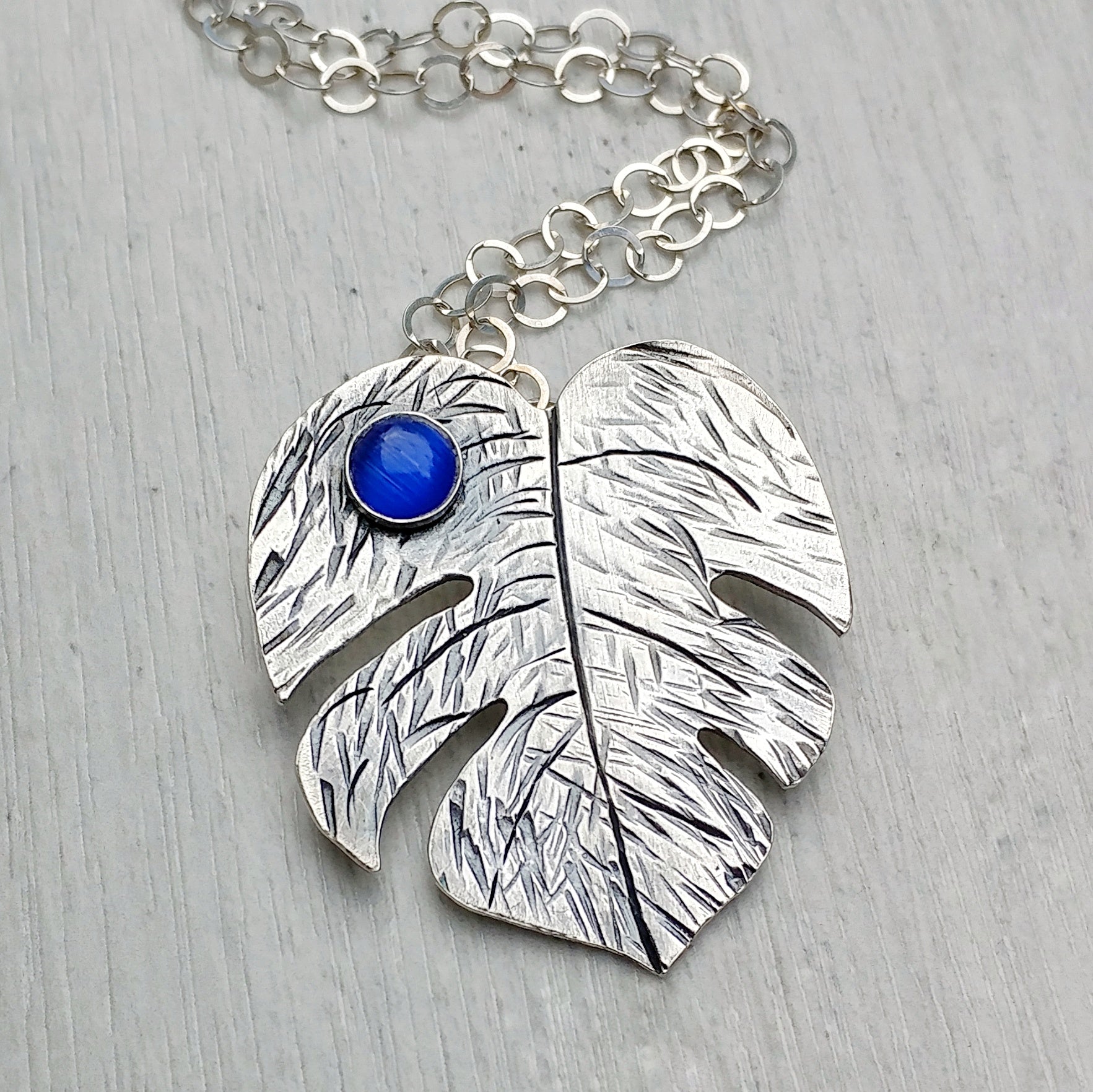 Sterling silver handmade monstera leaf Tiki necklace featuring various gemstones in this case a blue cats eye