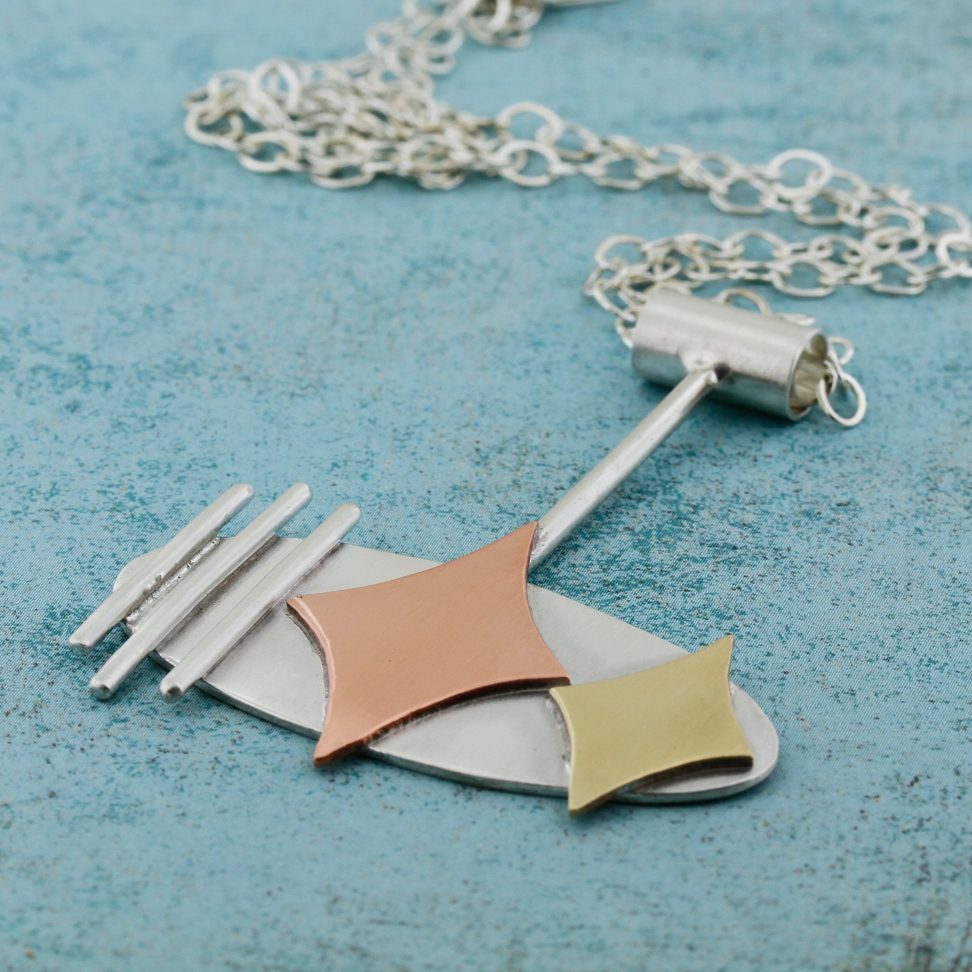 Mid century modern necklace handmade in sterling silver with copper and brass retro stars, and silver bars in an oval setting in a side view