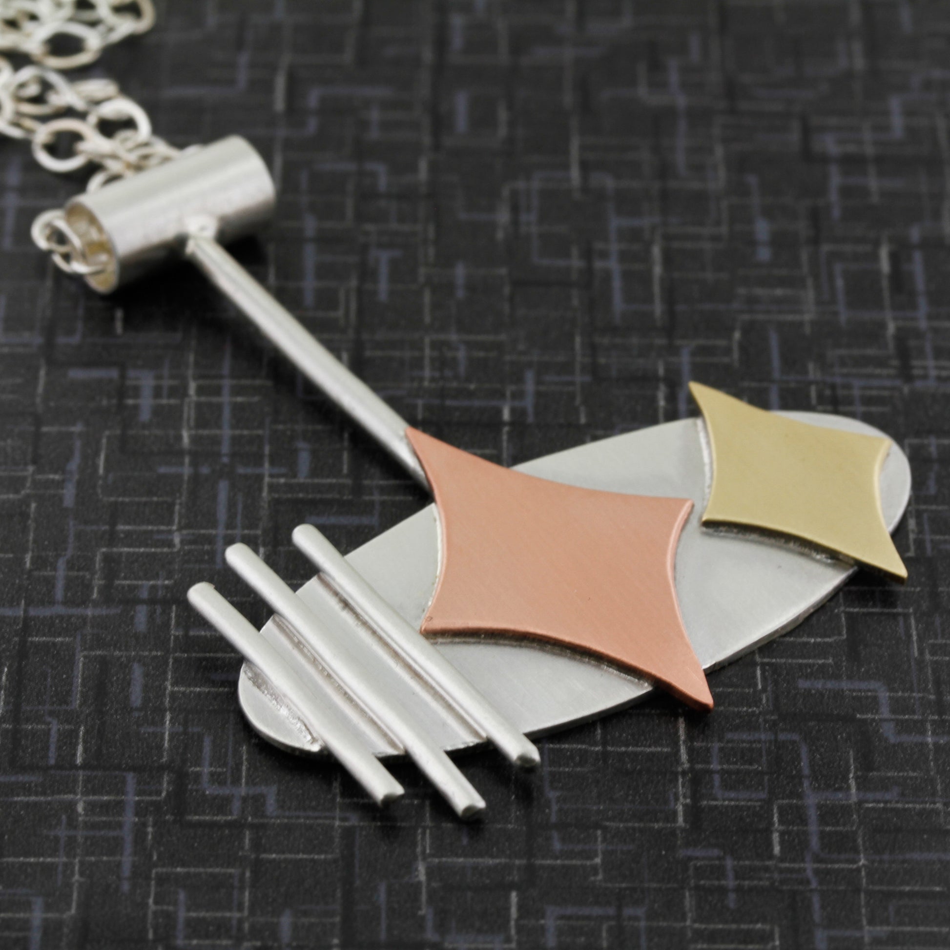 Side view of a Mid century modern necklace handmade in sterling silver with copper and brass retro stars, and silver bars in an oval setting