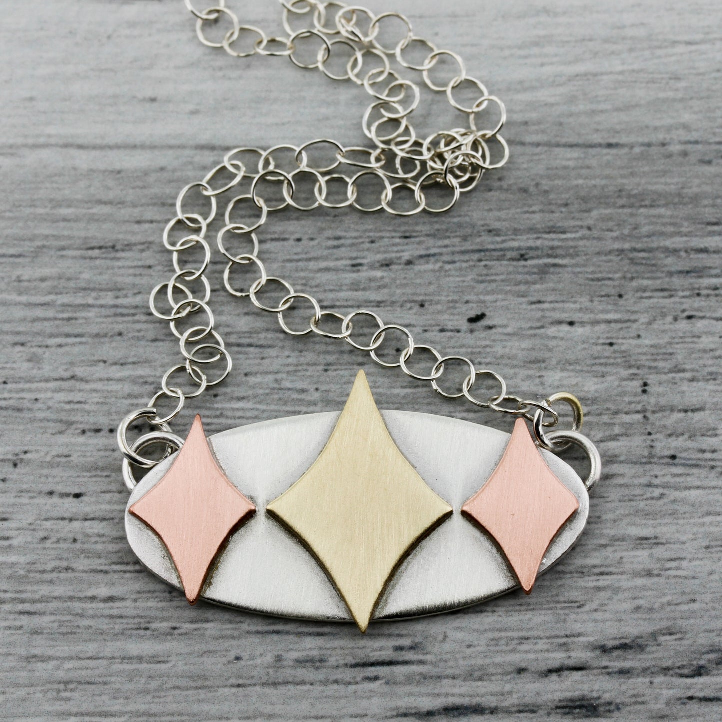 Mid century modern necklace handmade in sterling silver with copper and brass retro stars in an oval setting on a gray background