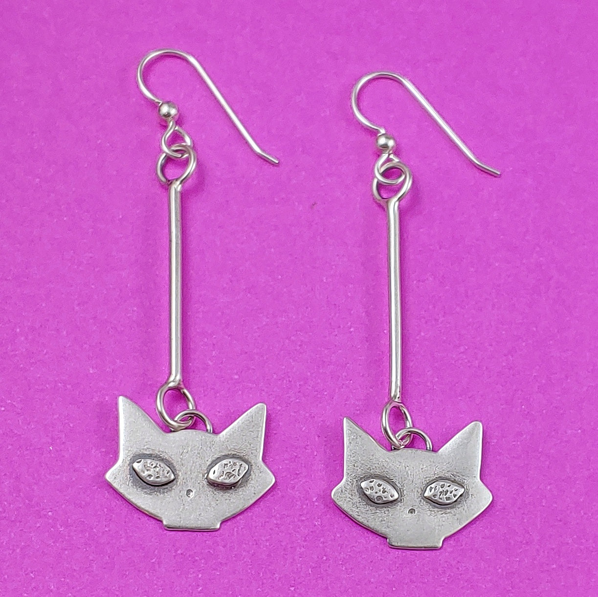 Mid century modern kitty head dangle earrings on pink background.