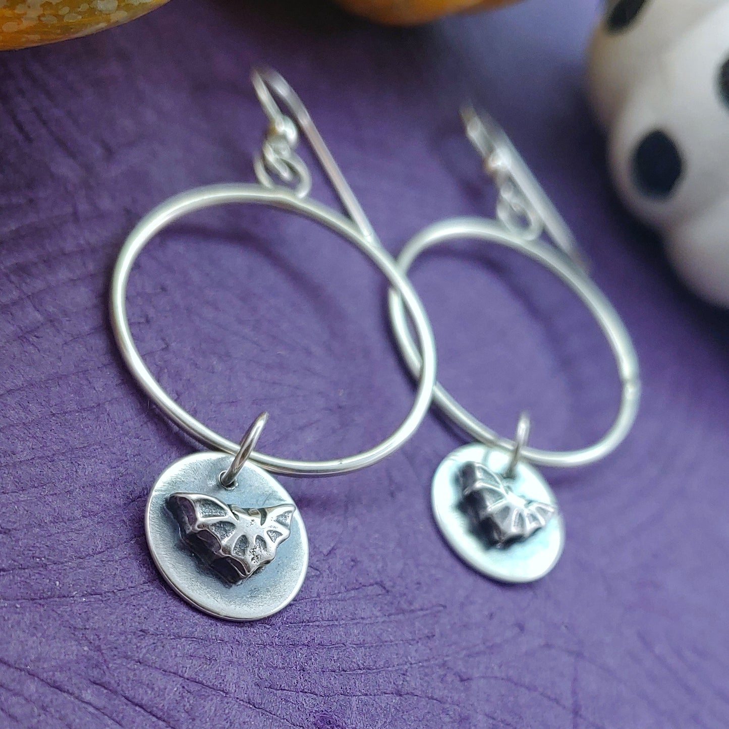 Sterling silver hoops with raised bat dangles shot on an angle on purple background.