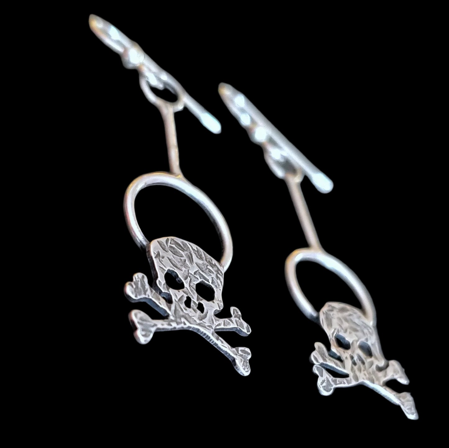 Close up view of the hammered sterling silver skull earrings on a black background.