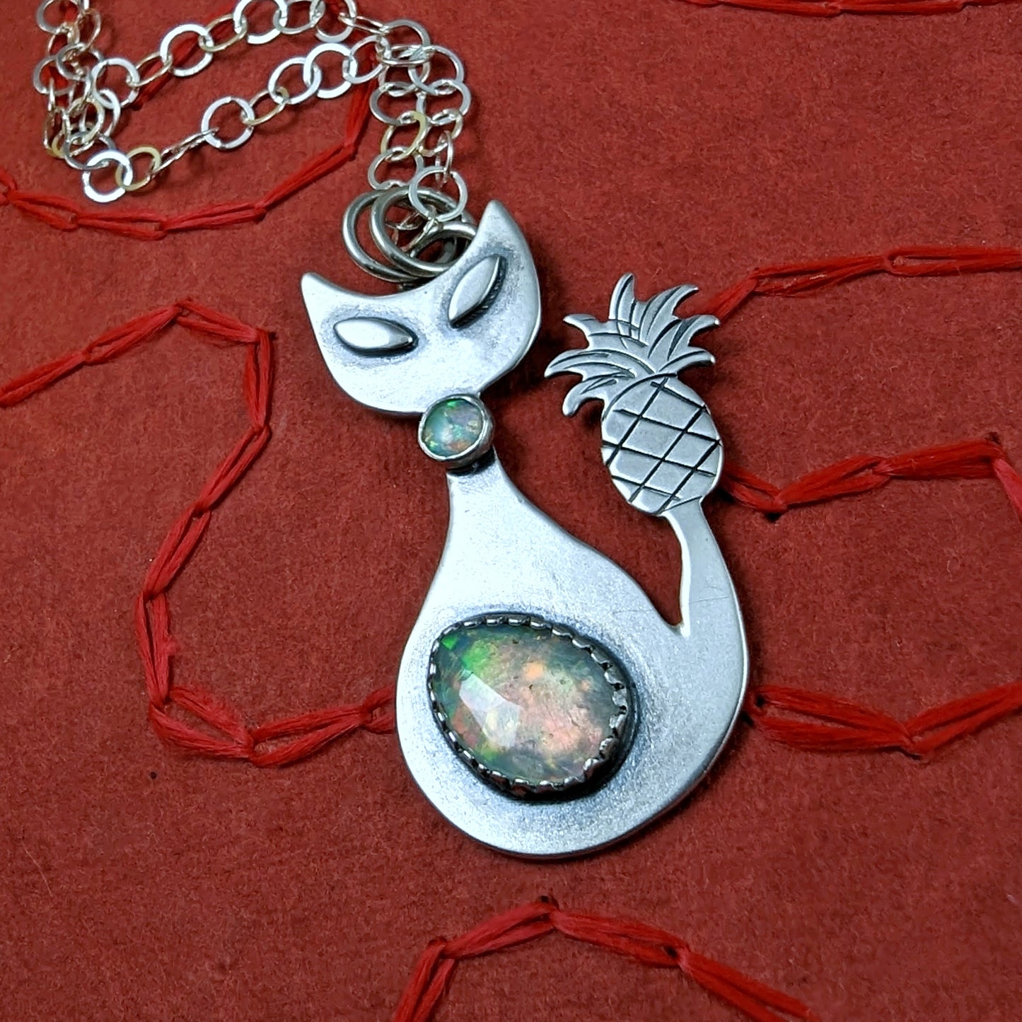 Sterling silver handmade cat with pineapple tail and Ethiopian opal on a red background