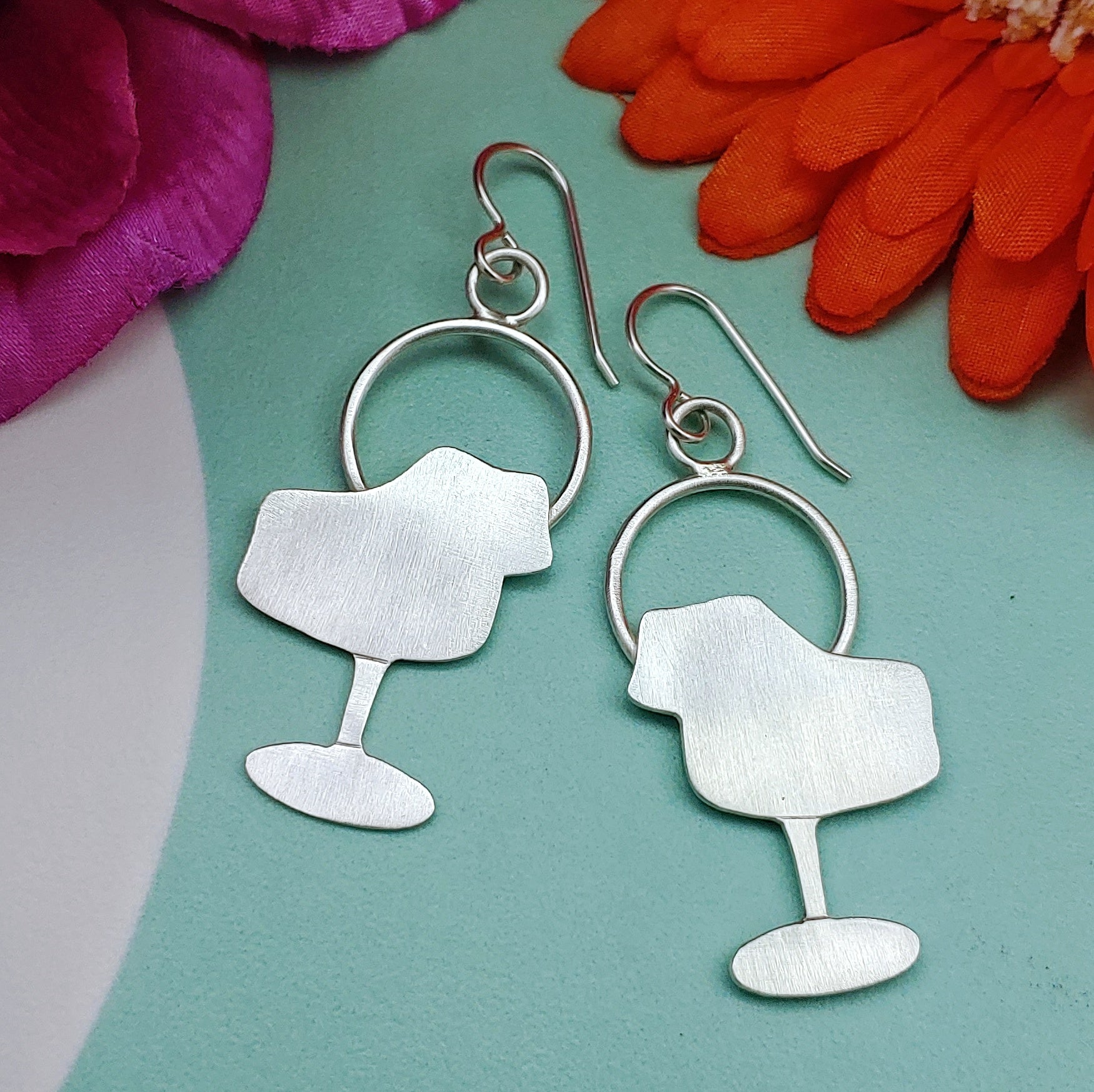Mid century modern tulip chair earrings handmade in sterling silver which are perfect for the 17th wedding anniversary gift of furniture as shown on a light teal background with flowers.