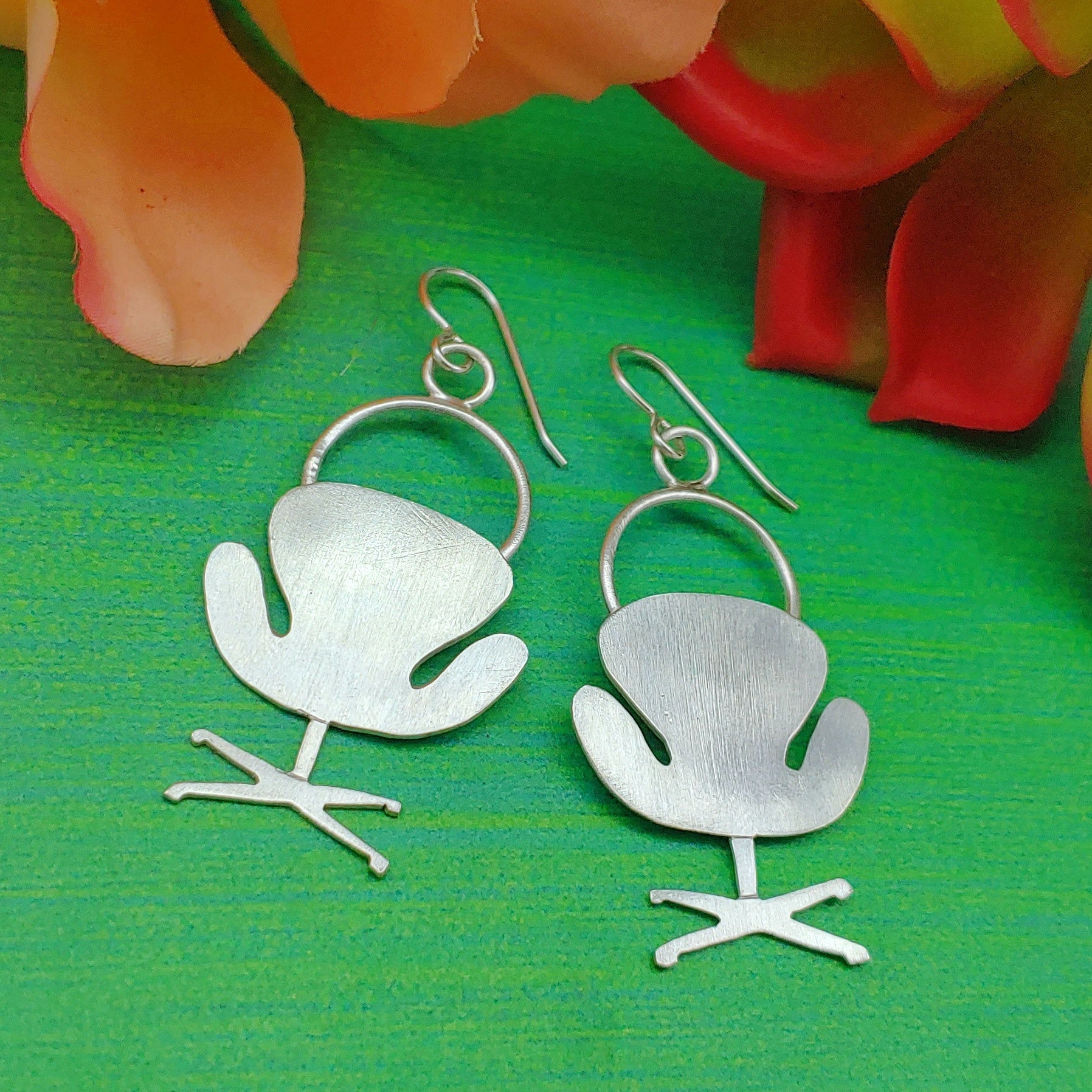 Mid century modern swan chair earrings handmade in sterling silver which are perfect for the 17th wedding anniversary gift of furniture as shown on a green background with flowers